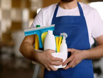 A man in an apron is holding a bowl of cleaning supplies.