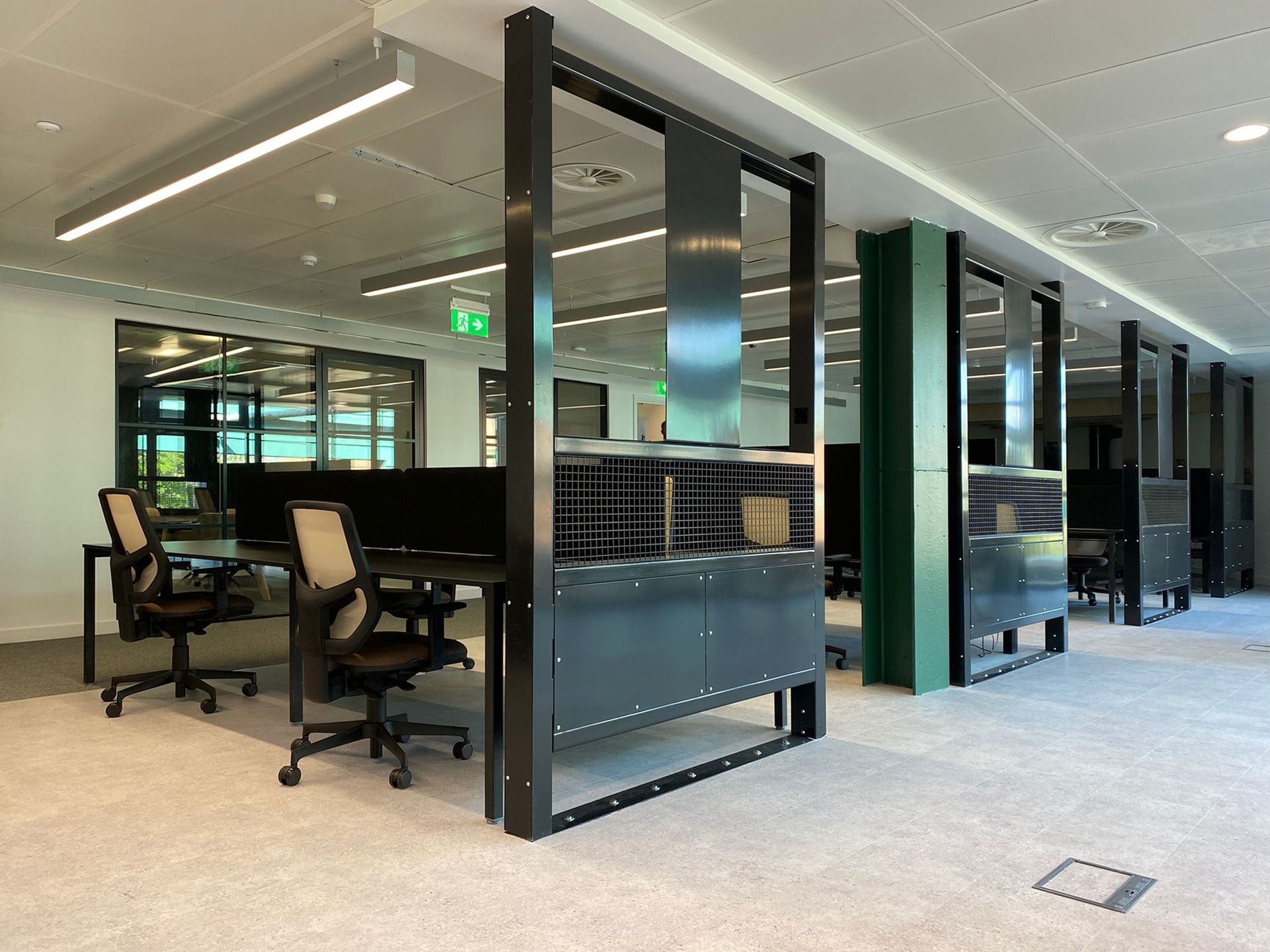 Rows of desks along an open space. The desking is black with space for two office chairs at each section. There are 16 sections in total. The desks have dividers to offer privacy while working or studying.