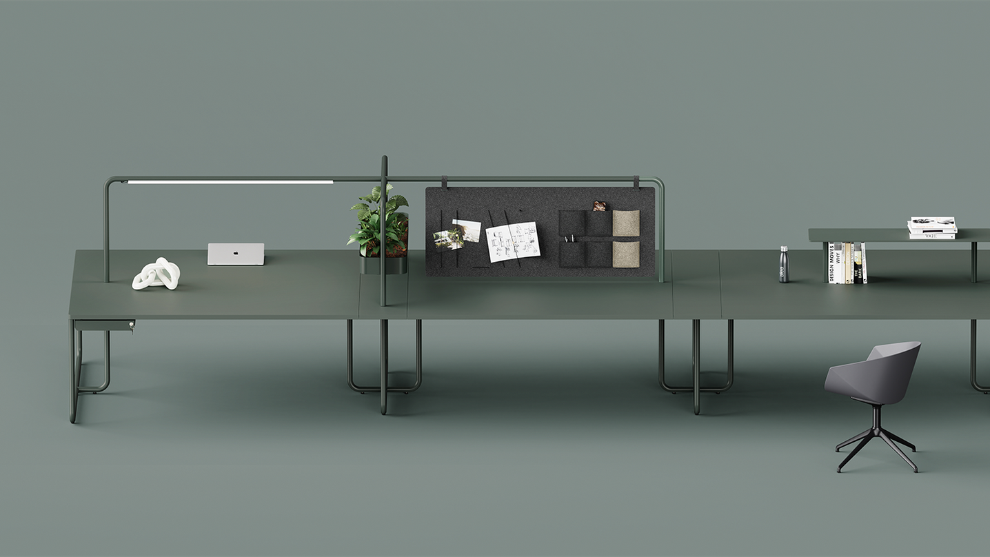 Alea Itube back to back bench desking with integrated fabric screen, lighting and shelves. The desk is a dark green. The backdrop is a green-grey colour. 