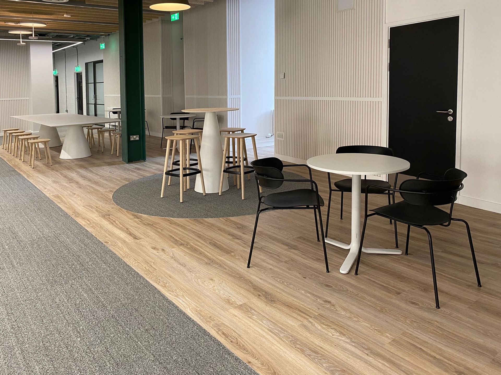 Alternative view of the dining area, featuring a white conference table with low stools, a tall circular table with high stools, and lower circular tables with dining chairs.