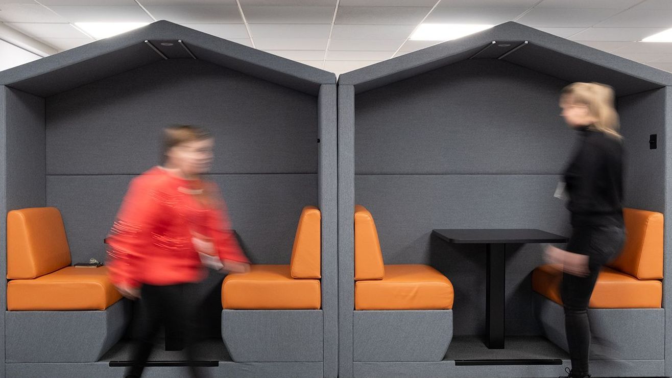 Two grey acoustic booths side by side. They have an angled top and are finished in a grey fabric with orange seats. Each booth has a black table in the middle.
Office furniture scotland