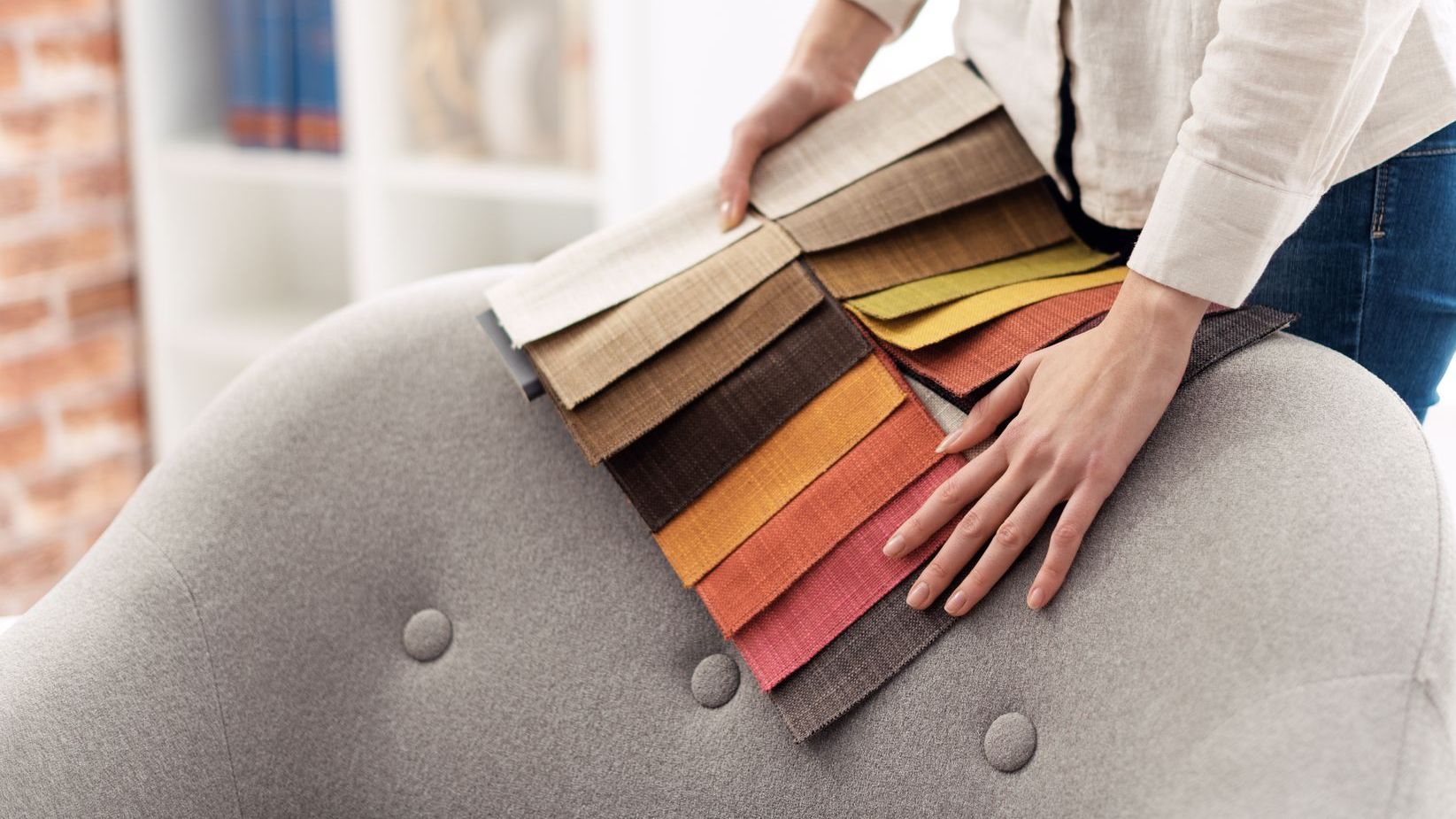 Woman holds swatches of fabric over an old sofa that she is getting reupholstered