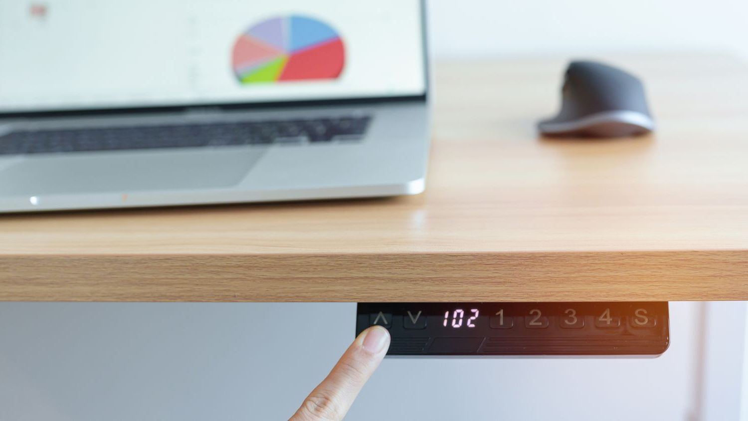 A finger pressing the adjustable buttons on a height-adjustable desk to raise and lower the desk. 