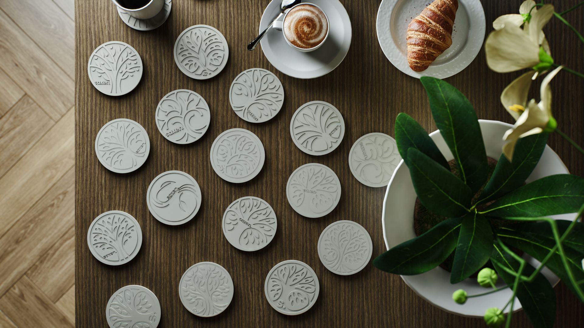 Range of Saxen's custom coasters on a table next to coffee and a croissant, in an overhead shot. 