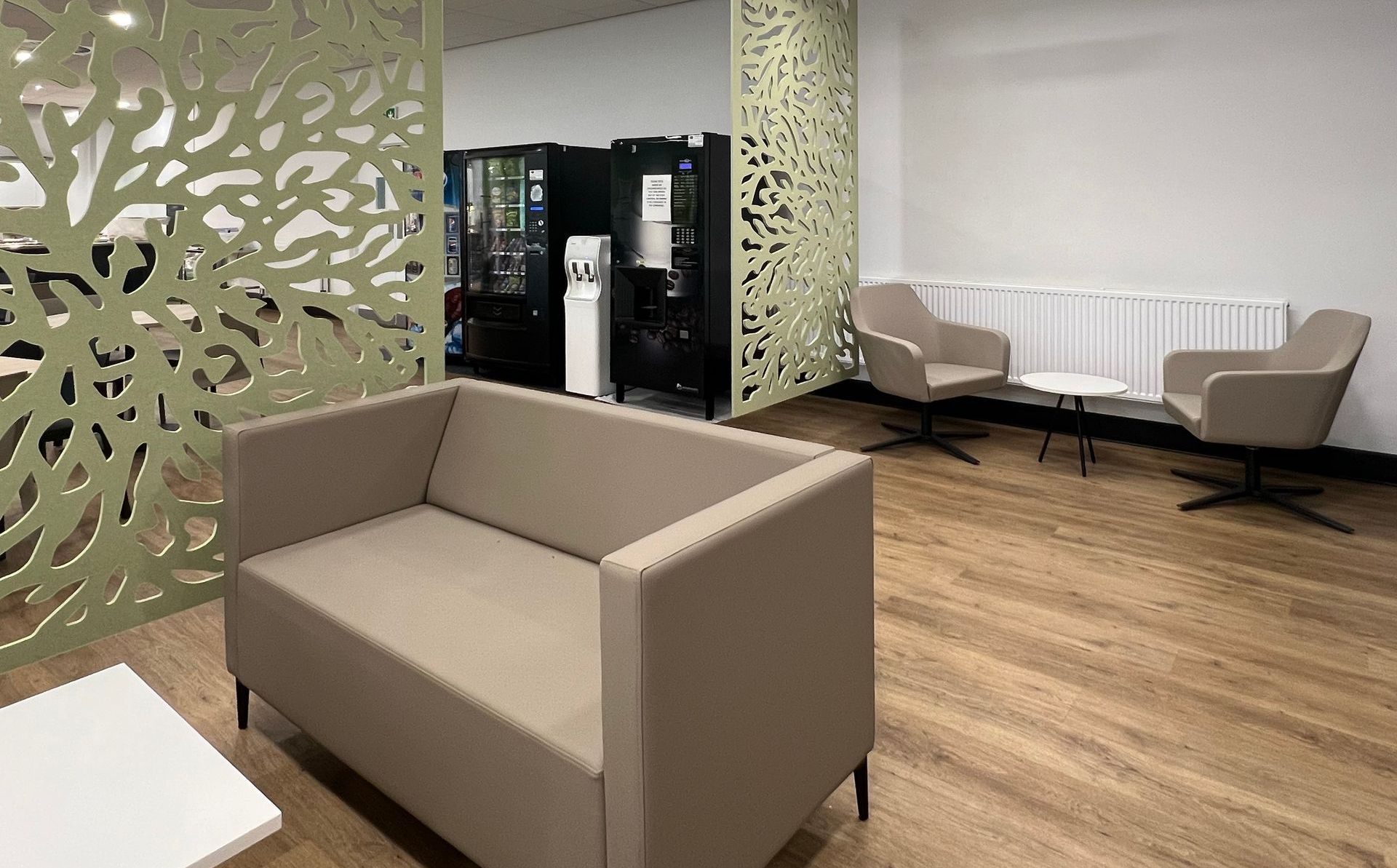 Autex acoustic ceiling-hung screens in a modern canteen space with soft seating, coffee table and planters. Vending machines are in the background.