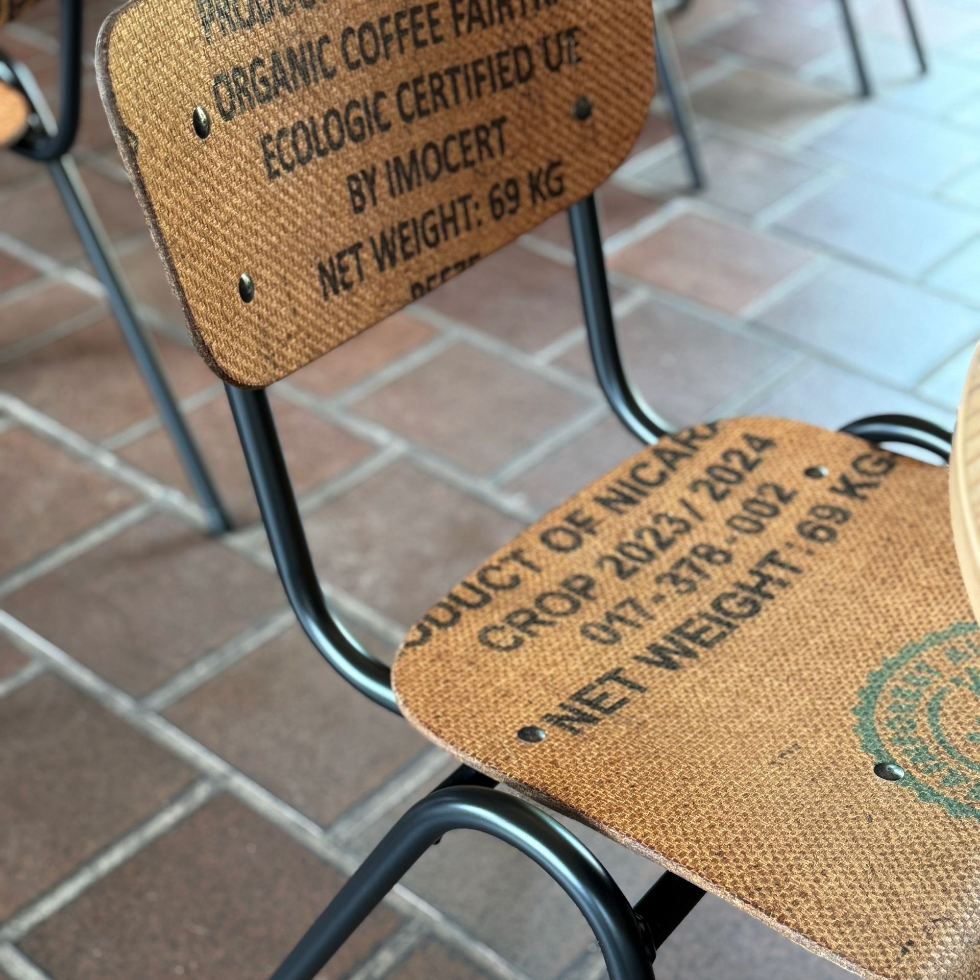 Chair made from a repurposed coffee bag. The black frame holds the seat and back, printed with text.