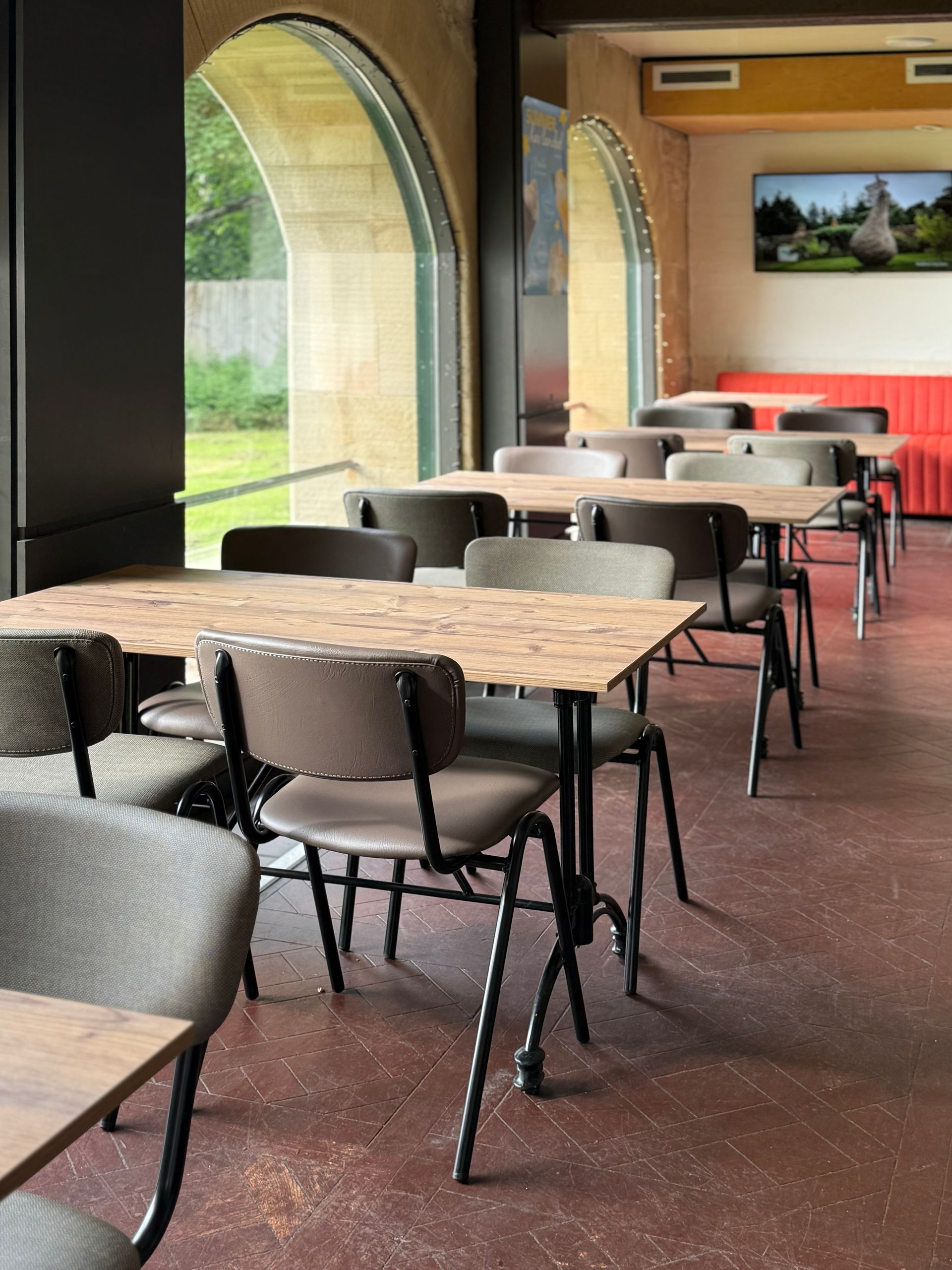 Empty restaurant dining area with tables, chairs, arched windows, and red floor.