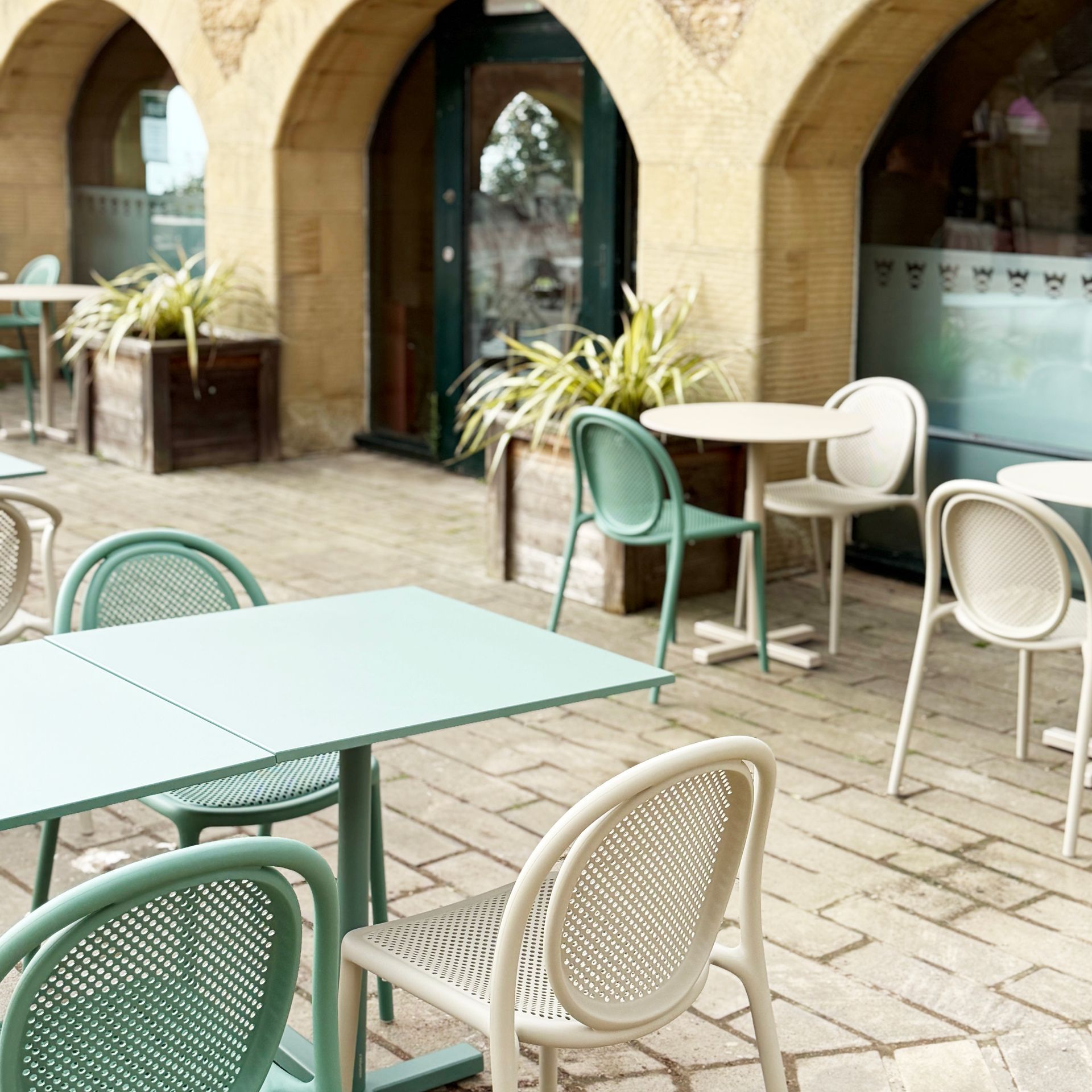 Outdoor cafe seating with turquoise and cream chairs and tables, under arches.