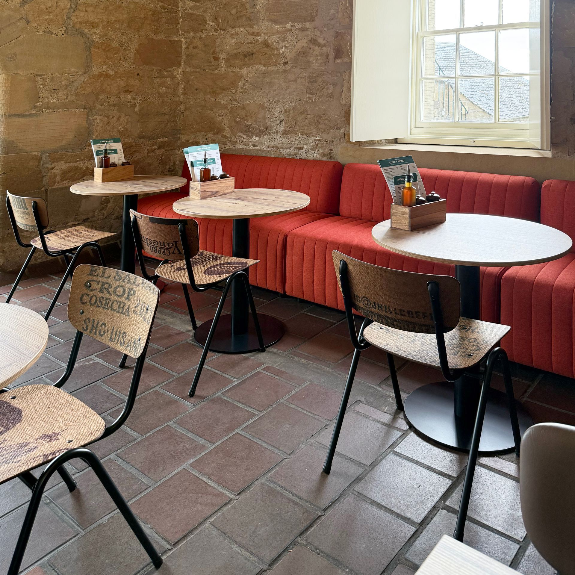 Cafe interior with round tables, vintage chairs, a red bench, and a brick floor.