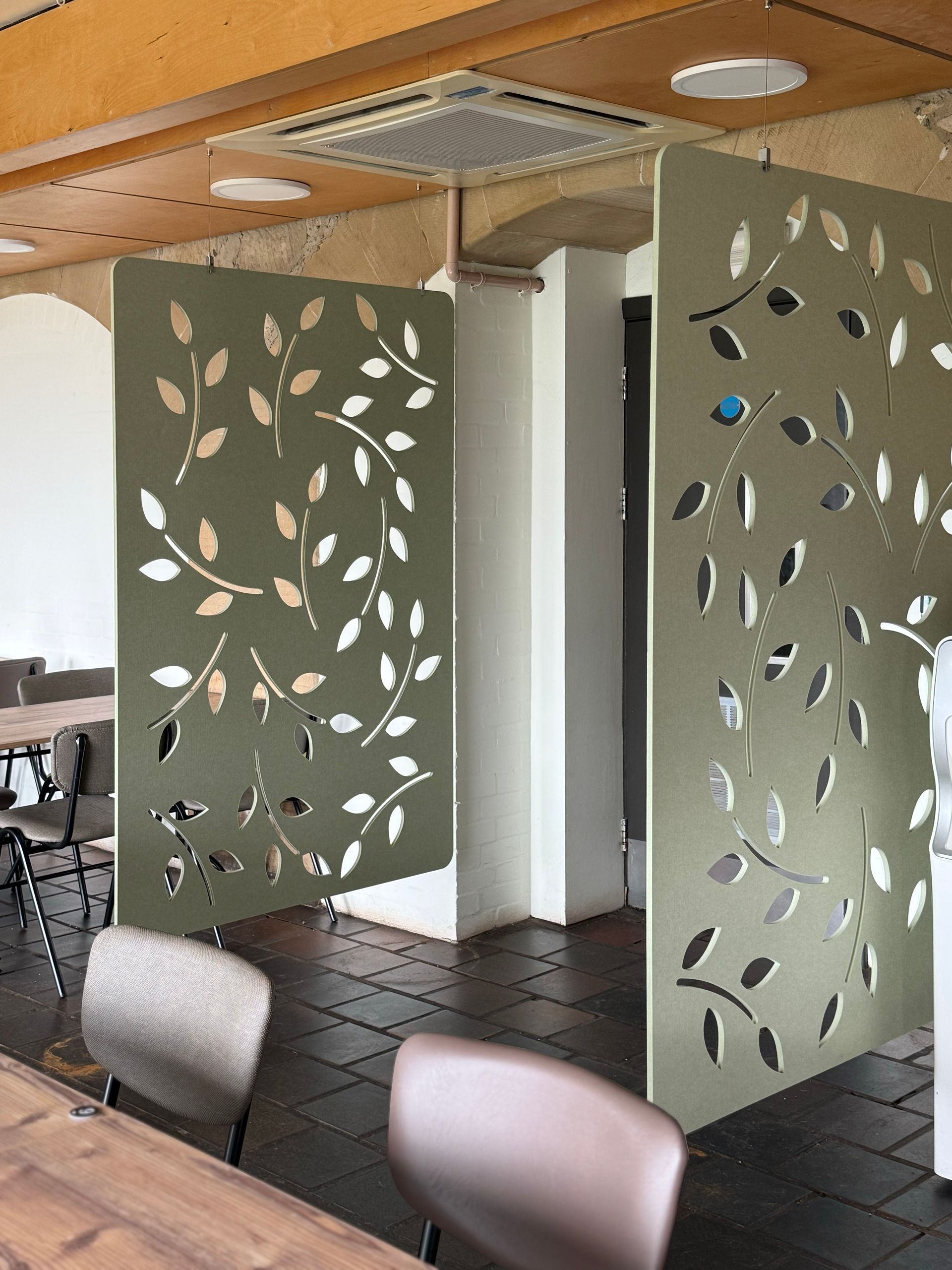 Olive green decorative leaf-patterned room dividers in a dining area with tables and chairs.