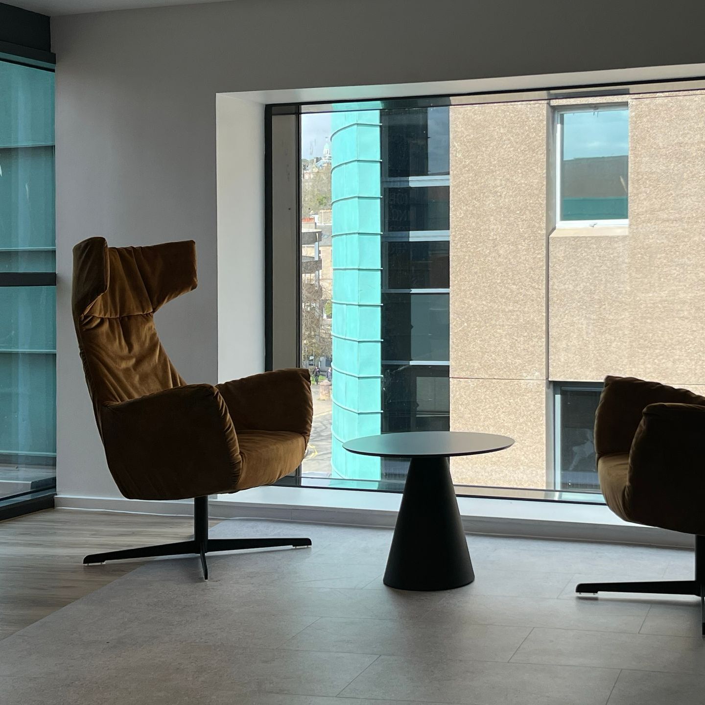 Large wing armchair upholstered in a mustard-yellow colour, placed nearby a large window with a view of the city.