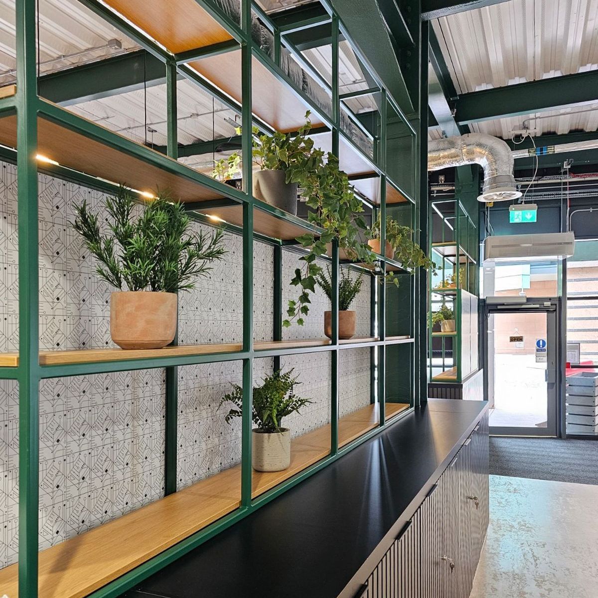 Close up of the storage divider with cabinets and shelving for plants. It has light wooden shelves and green metallic structure. 