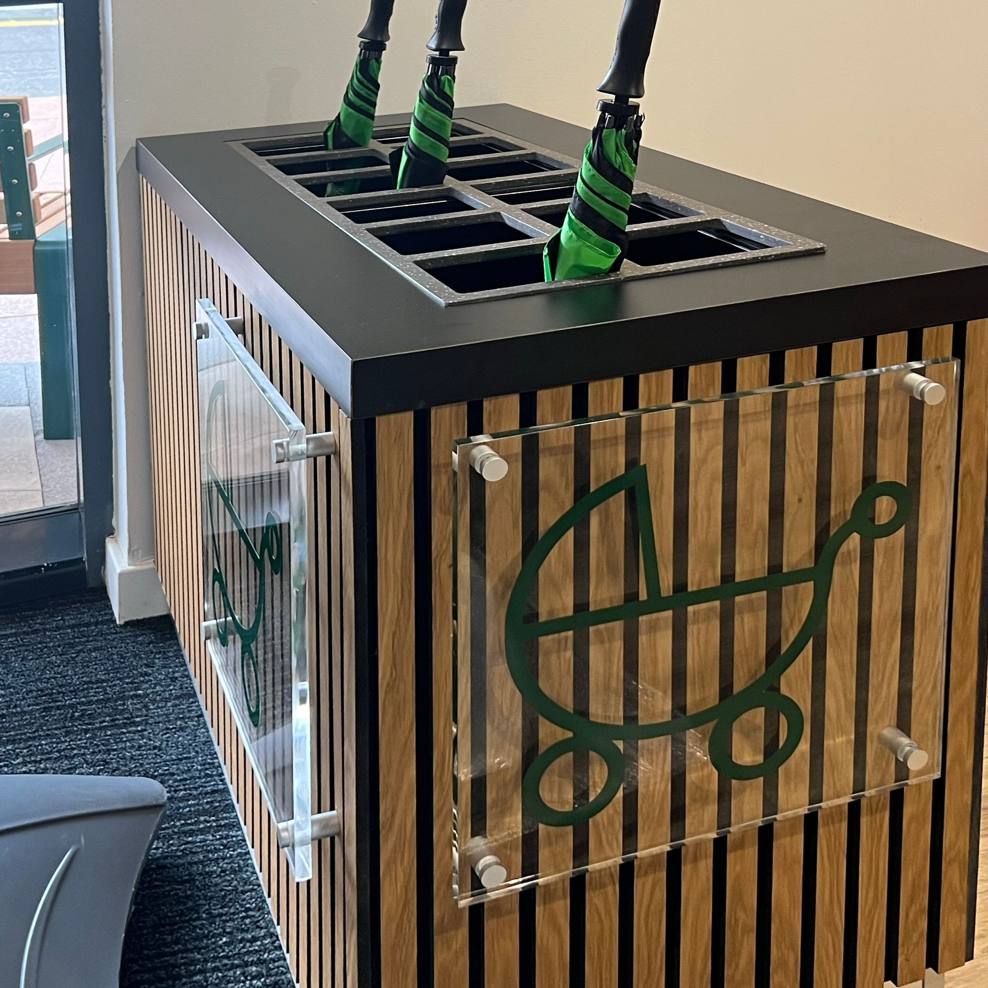 A wooden panelled storage space for people to leave their umbrellas and park their prams.