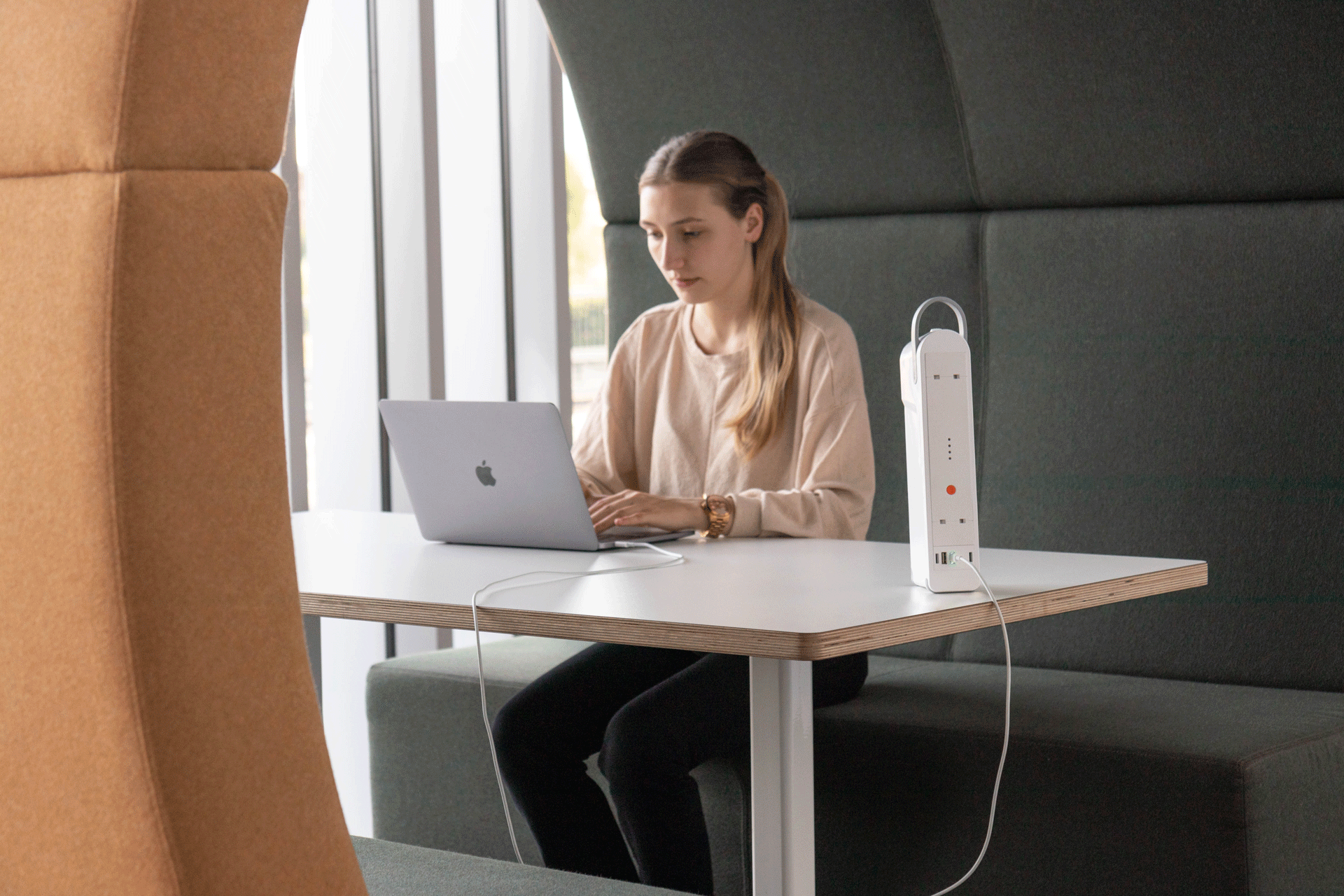 A woman sitting at a desk with a MacBook connected to a QikPac power supply which provides portable power. Saxen, commercial furniture specialists in Scotland, provide these portable power supplies. 