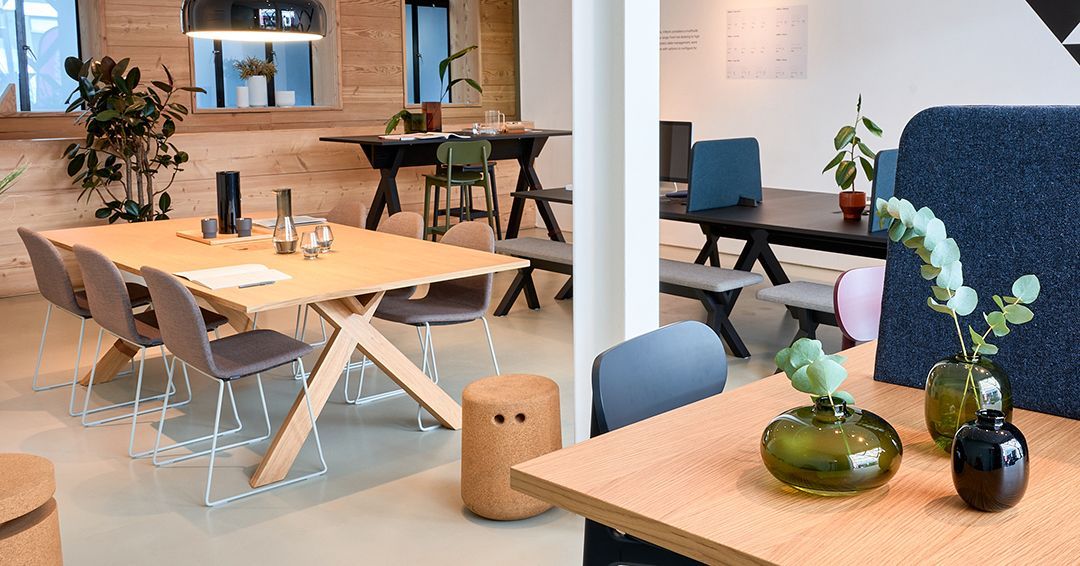 Office space with VWorktables in the office in oak, black, and varying heights. At each table are a collection of chairs or benches. 