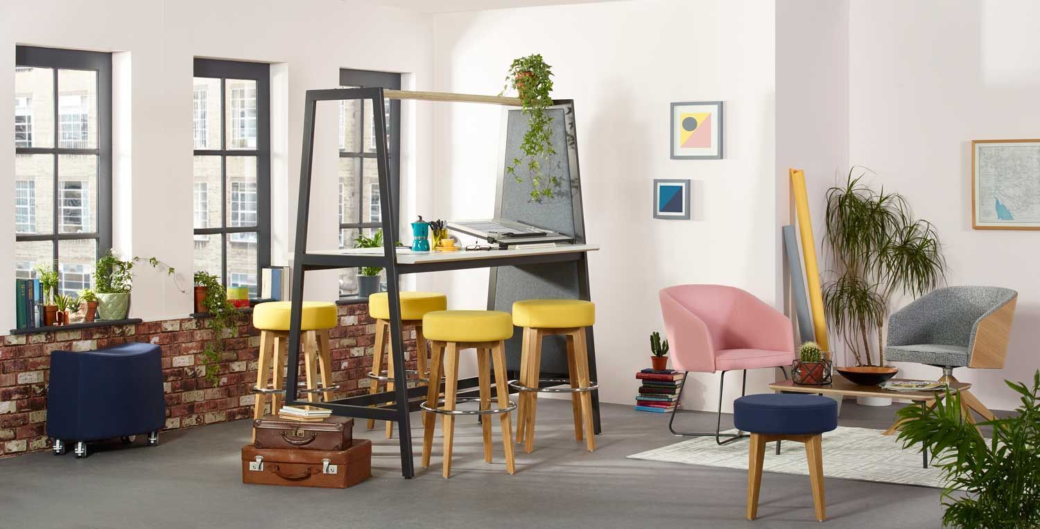 Room with an easel, yellow stools, pink chair, and plants.