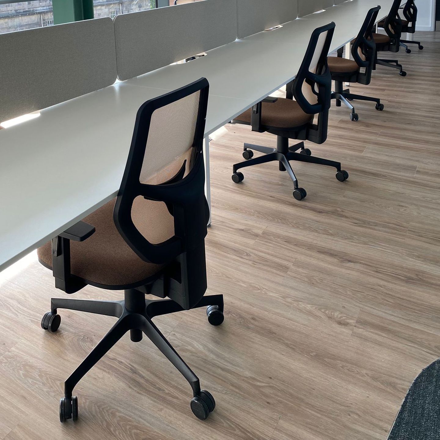 Ergonomic armchairs placed along a white bench desk with dividers.