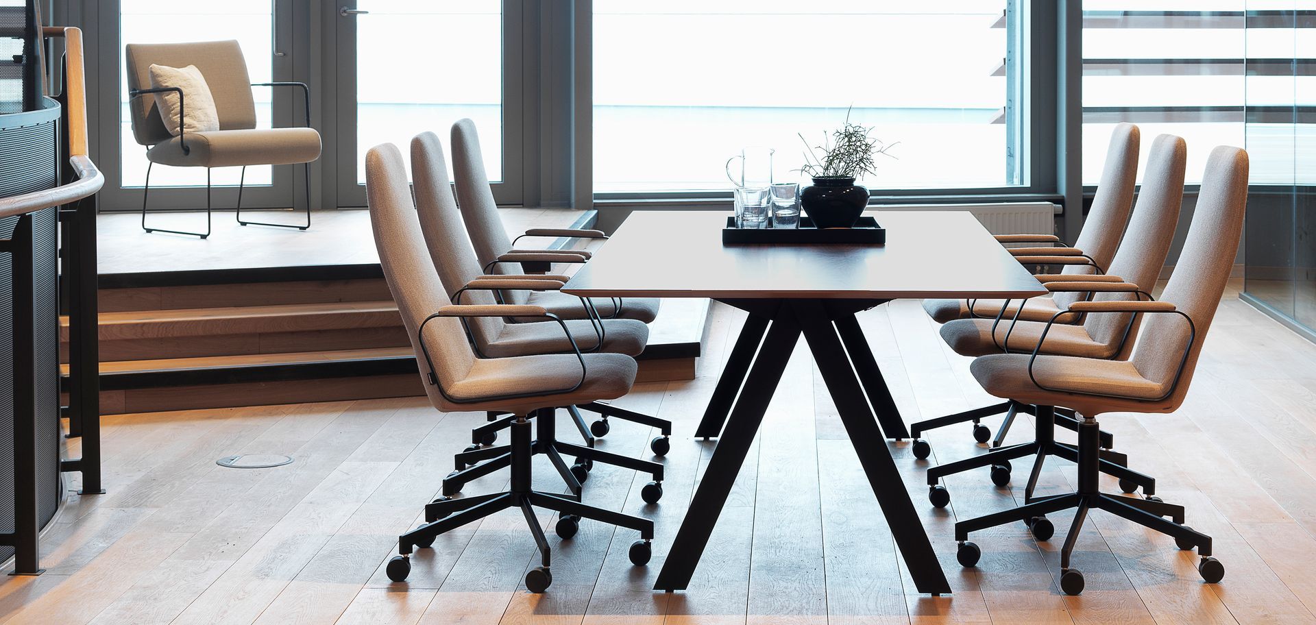 Modern office with conference table and chairs. Wooden floor, chairs are beige and black.