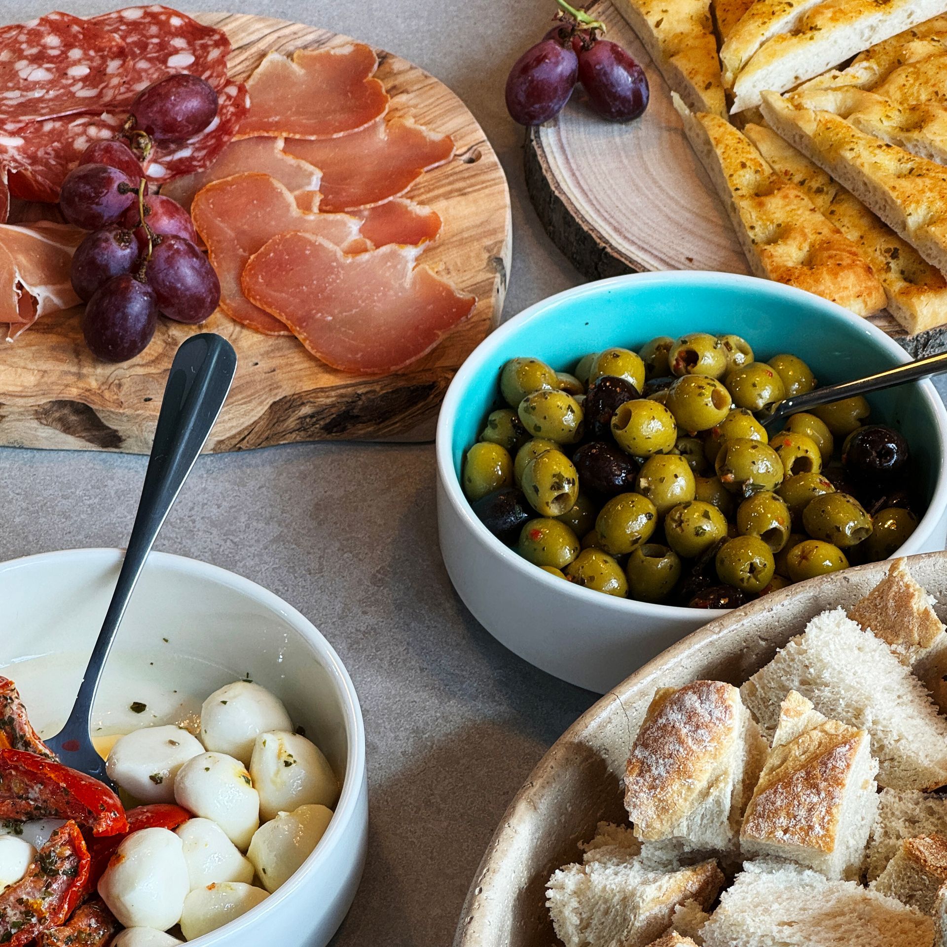 Charcuterie spread with meats, olives, bread, and grapes.