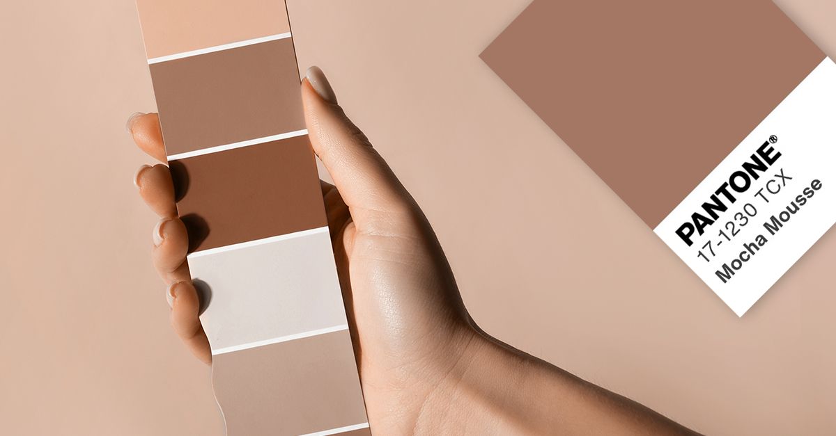 A person is holding a pantone color swatch in their hand showing Mocha Mousse the 2025 Colour of the Year