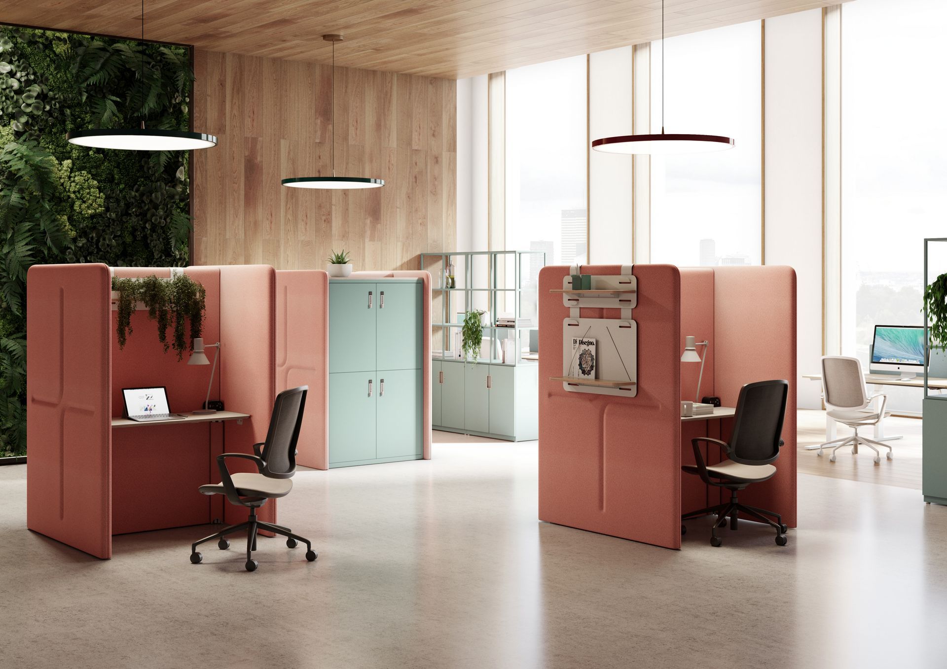 A spacious office with large windows letting in natural light. There are a few private booths in a peach-tone. At the booths are a laptop and chair. In the background are beautiful blue dividers with storage, plants and books. 