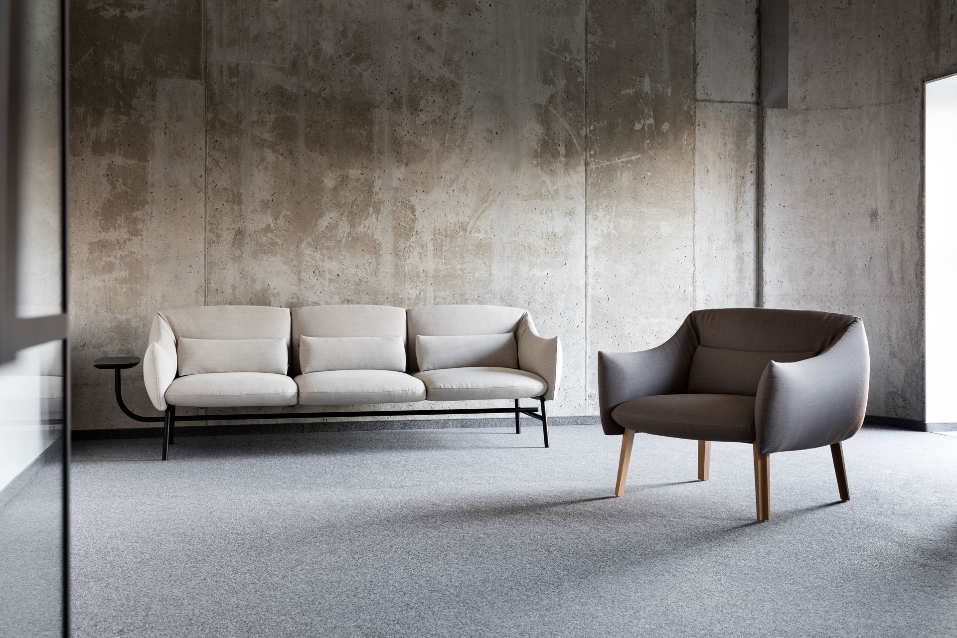 Modern living room: Beige sofa and gray armchair against textured concrete walls, on speckled gray carpet.