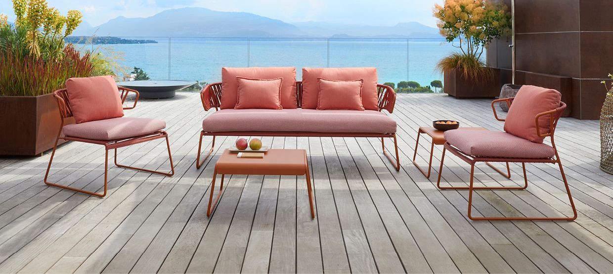 Hospitality outdoor furniture set in coral pink on a deck overlooking a lake and mountains.