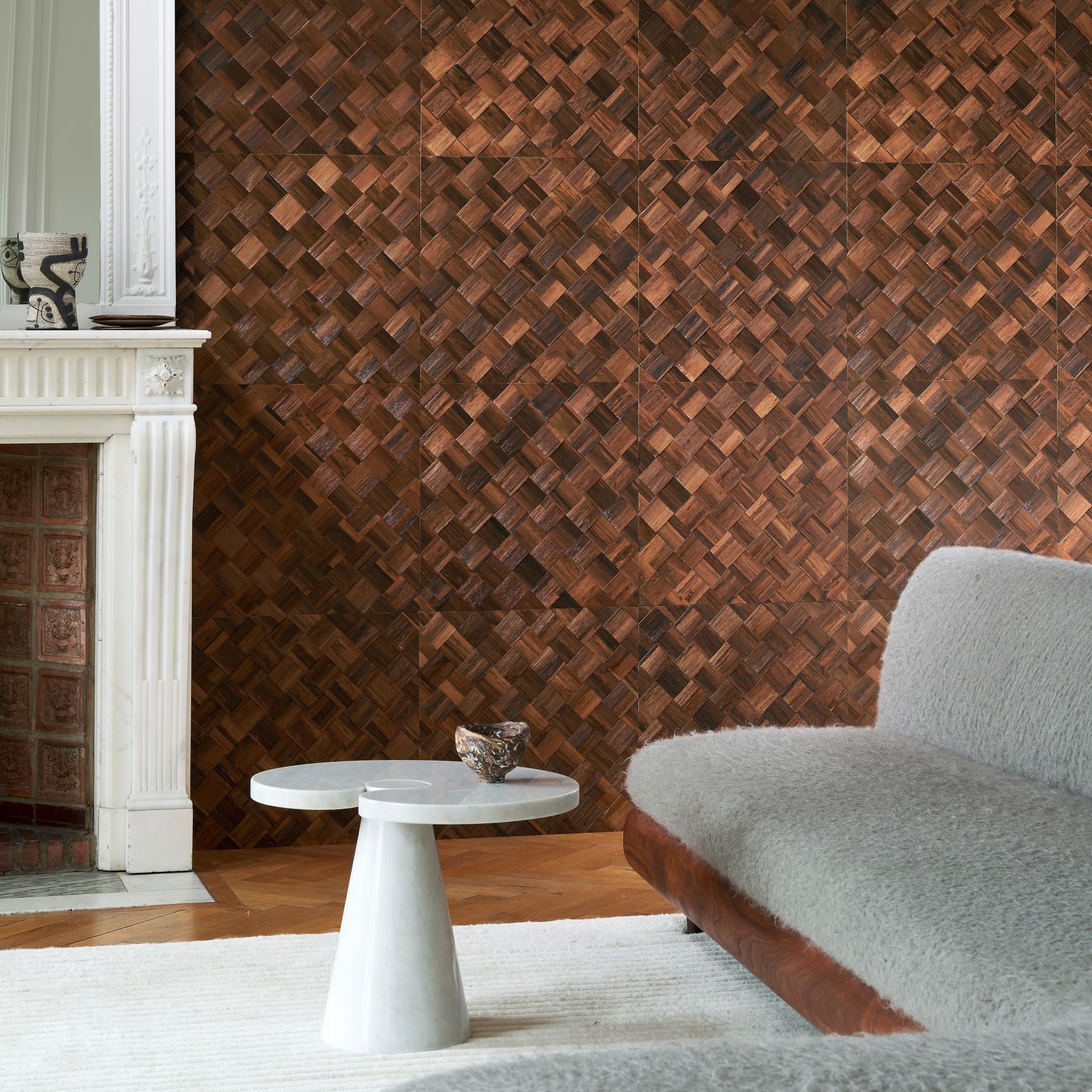 Living room with environmentally friendly woven banana leaf wall panels, white fireplace, gray sofa, and small white table.