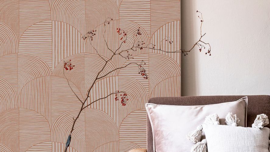 Peach-toned wallpaper in the background with a brown sofa in front of it and pink pillows. A berry tree stands before the wallpaper. 