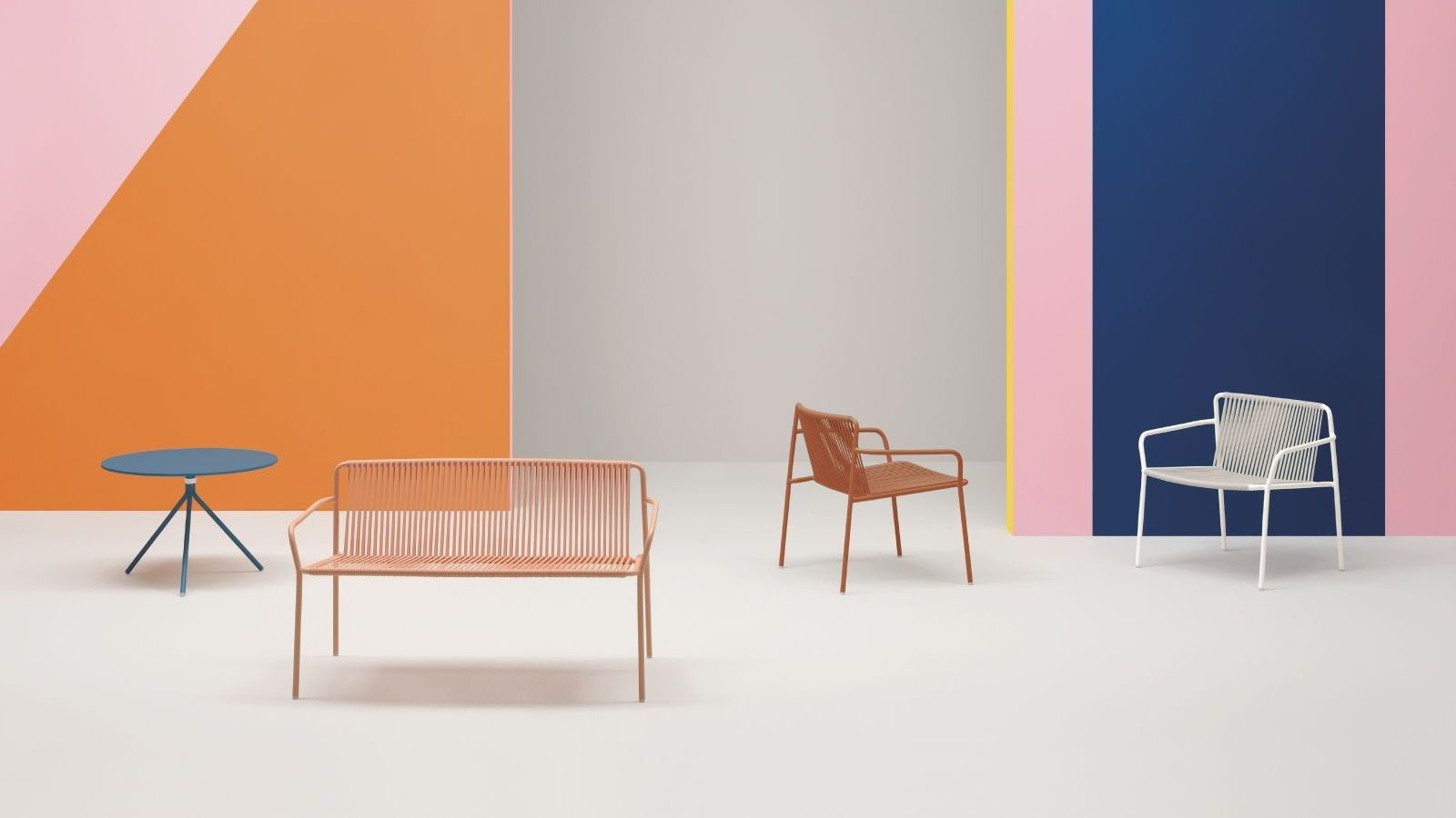 2 Pedrali chairs and 1 bench dotted around a large spacious room. There is a small table in the background too. The floors are white and the walls are pink, orange, yellow and blue. 