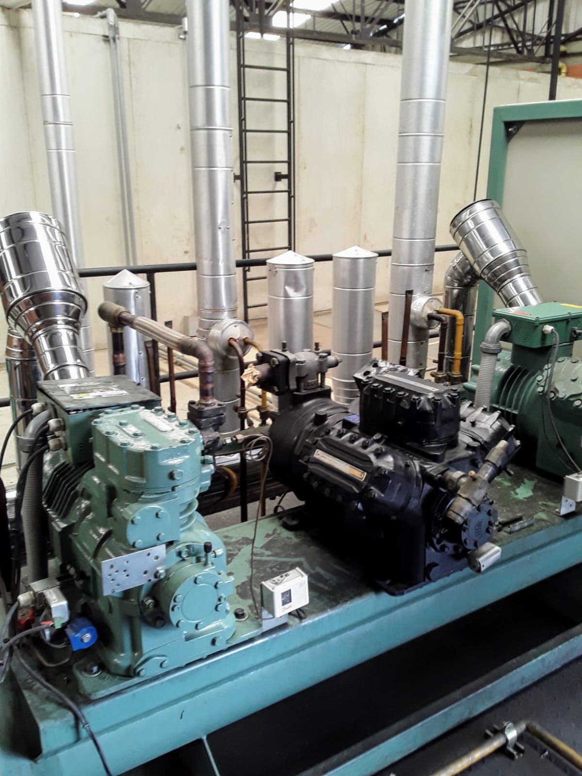 Equipo de refrigeración industrial con tuberías plateadas y compresores verdes y negros.