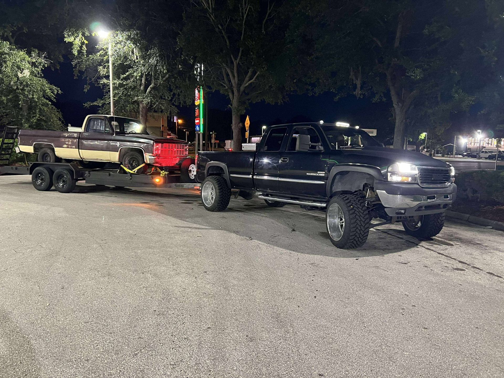 Dark pickup truck towing a lighter-colored truck on a trailer at night.