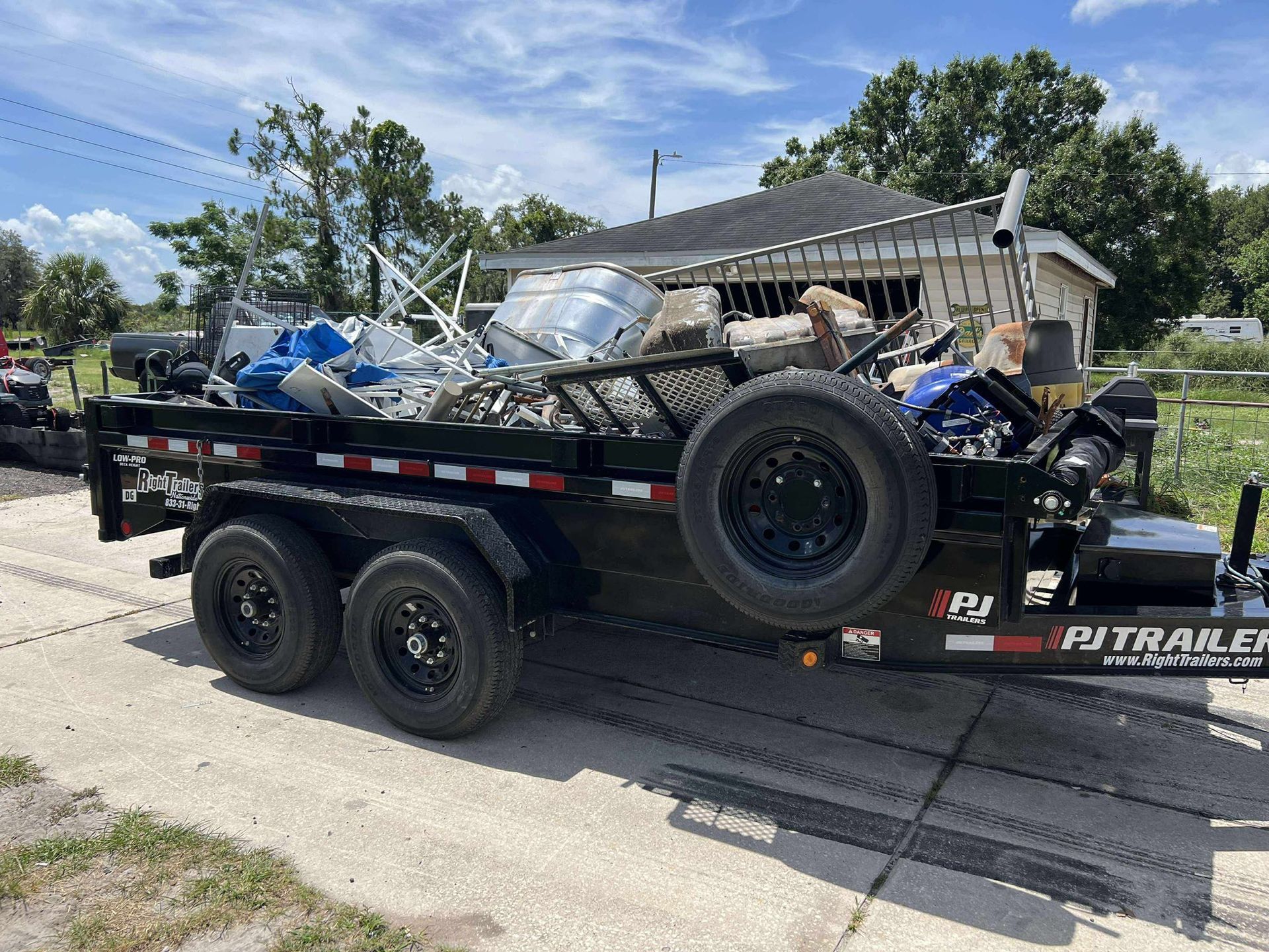 Black trailer loaded with scrap metal parked on a road in front of a house.