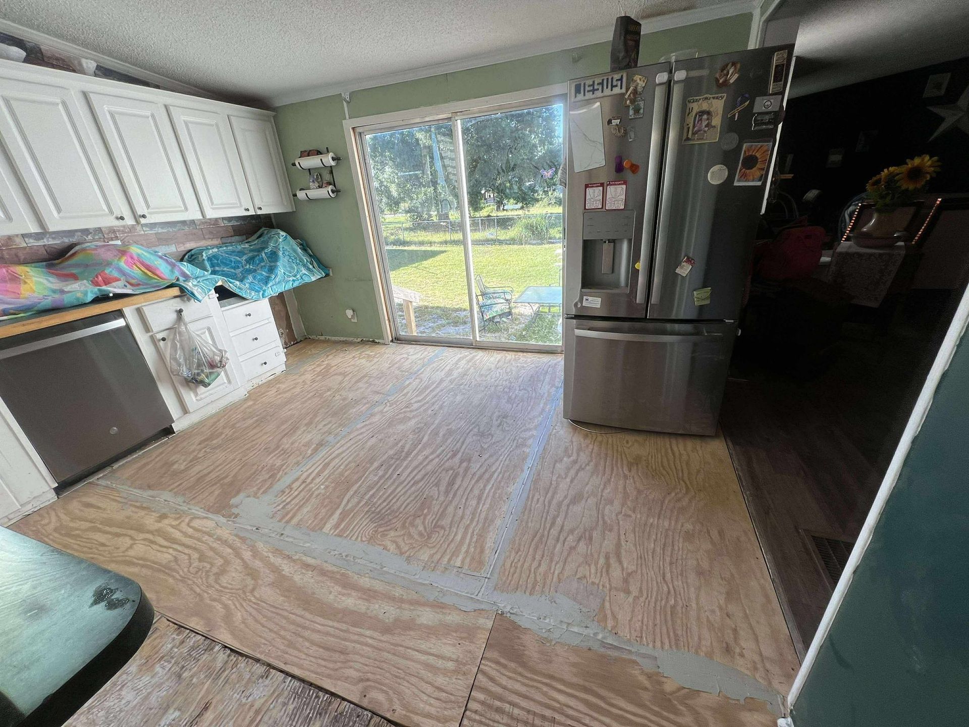 Kitchen with plywood flooring, appliances, and sliding glass door to backyard.