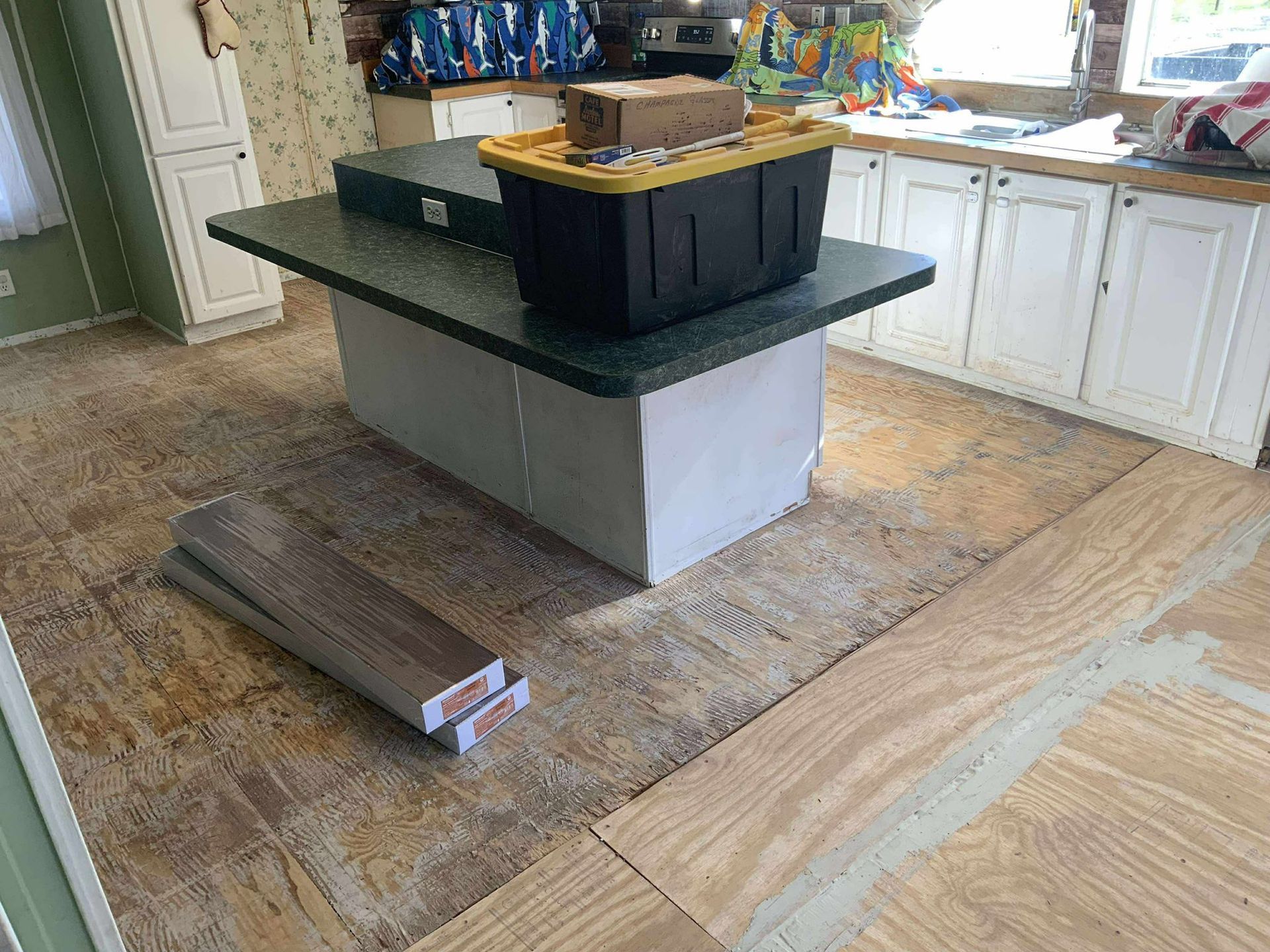 Kitchen with partially installed flooring; island with storage bin.