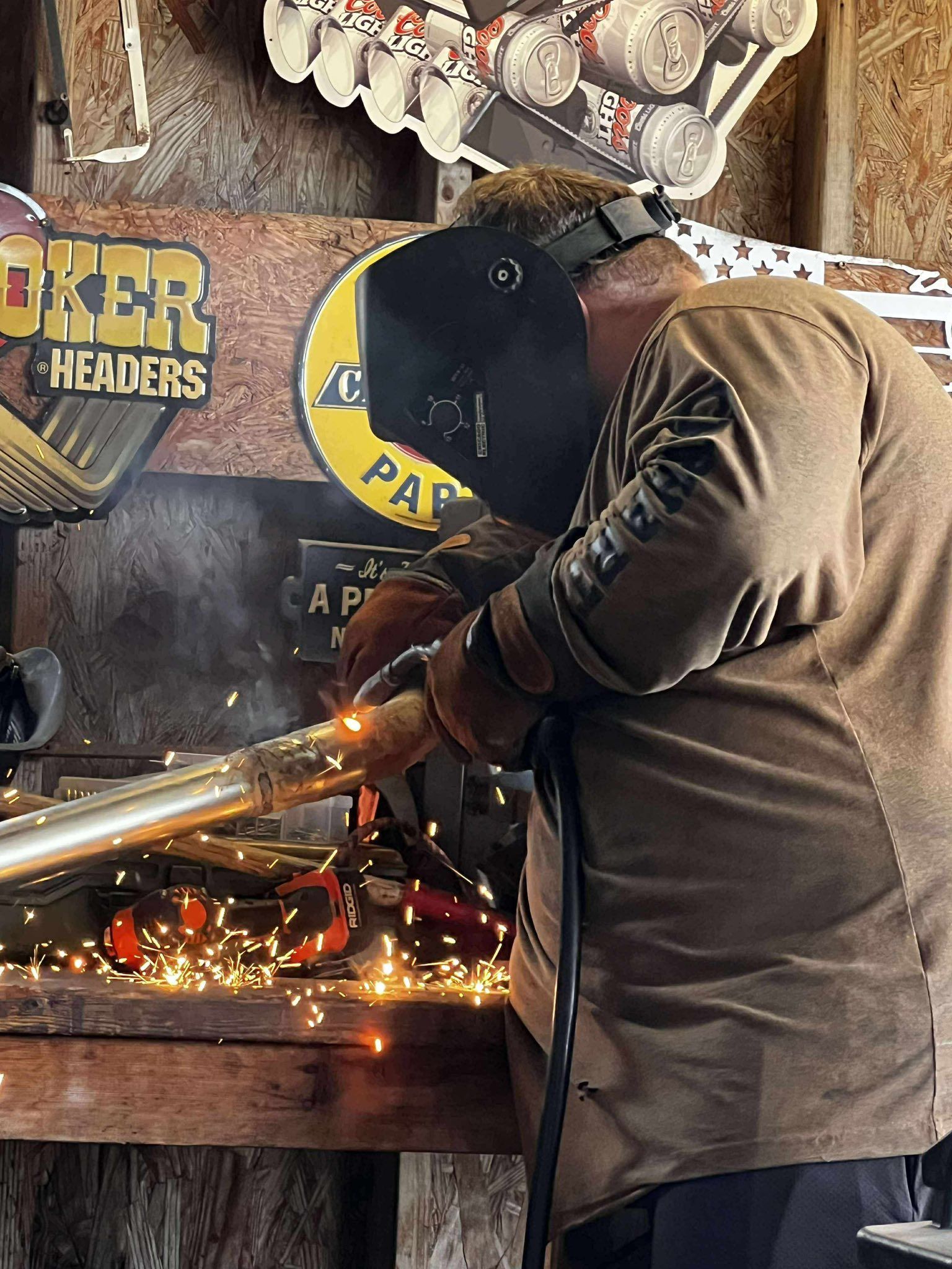 Man in welding gear welding metal, sparks flying, inside a workshop.