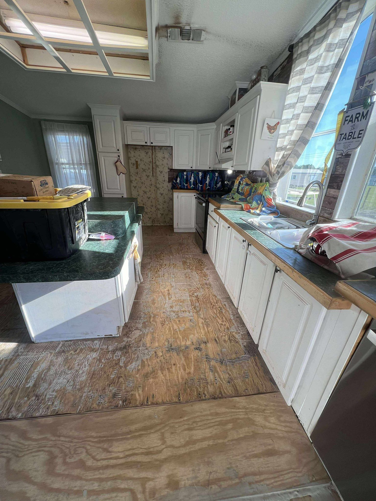 Kitchen with white cabinets, green countertops, and damaged flooring.