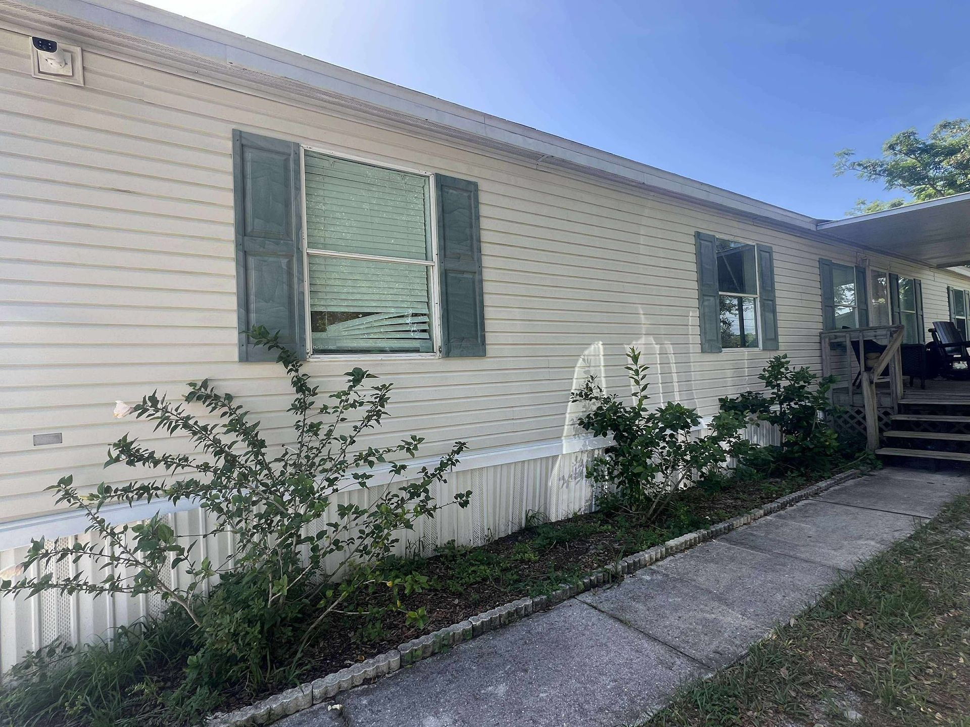 Mobile home with light siding, green shutters, and a walkway lined with bushes.