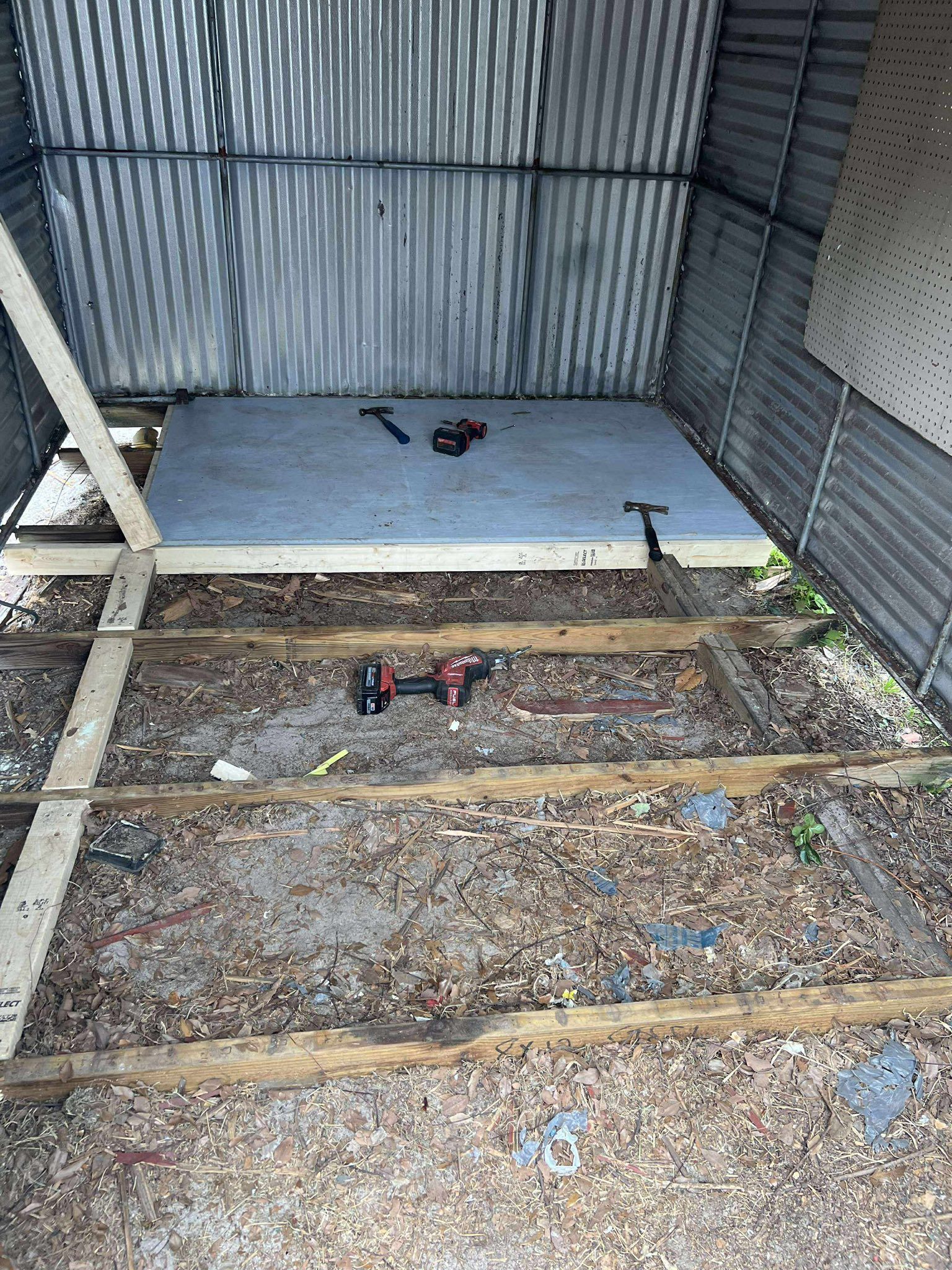 Interior of a corrugated metal shed under construction; tools on the floor and a partially built platform.