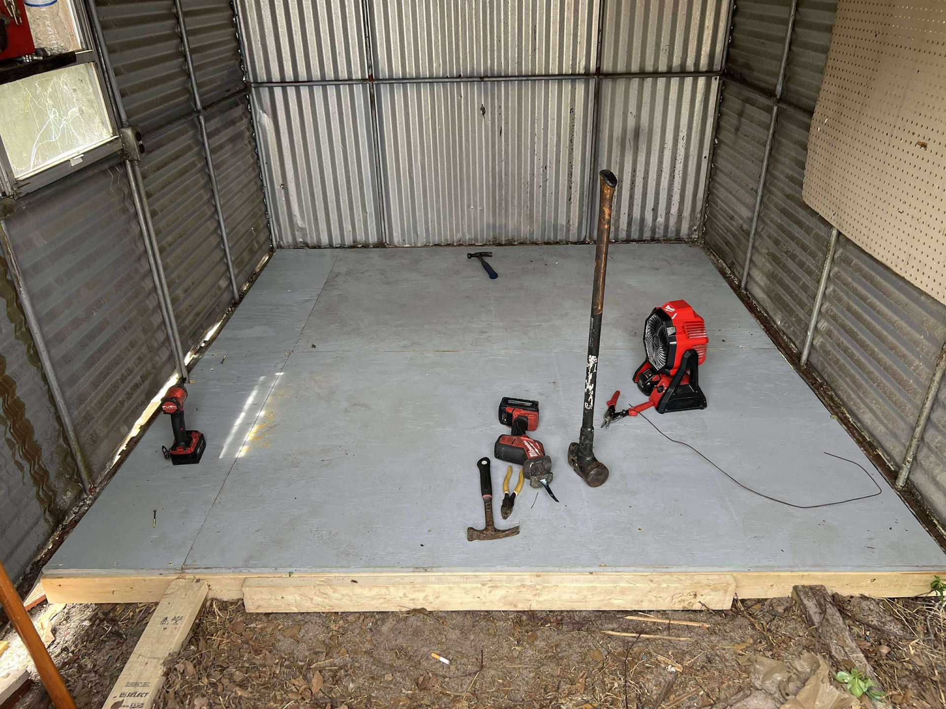 Inside of a metal shed with tools scattered on the gray plywood floor.