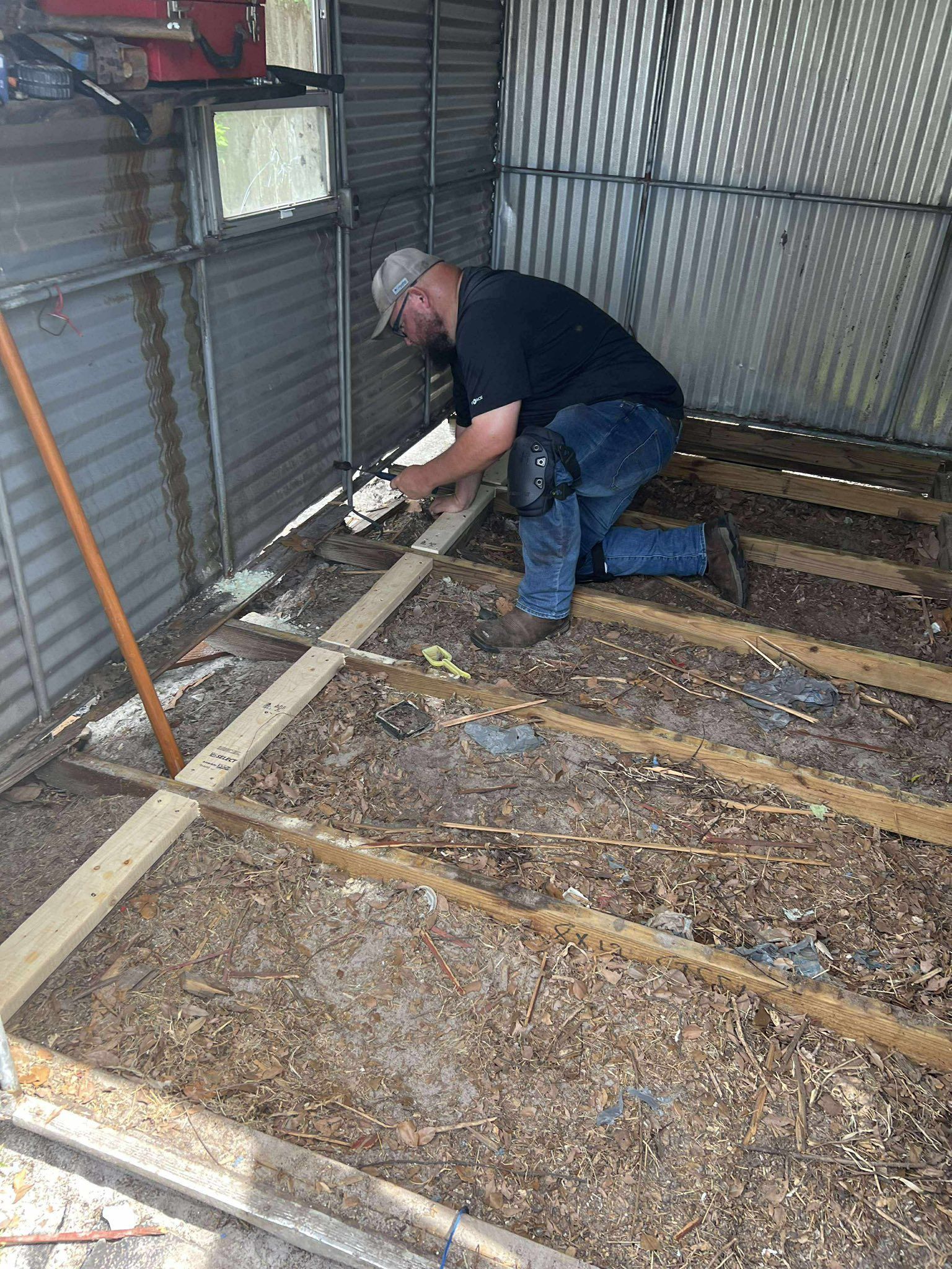Man installing wooden boards in a shed, kneeled with a caulk gun.