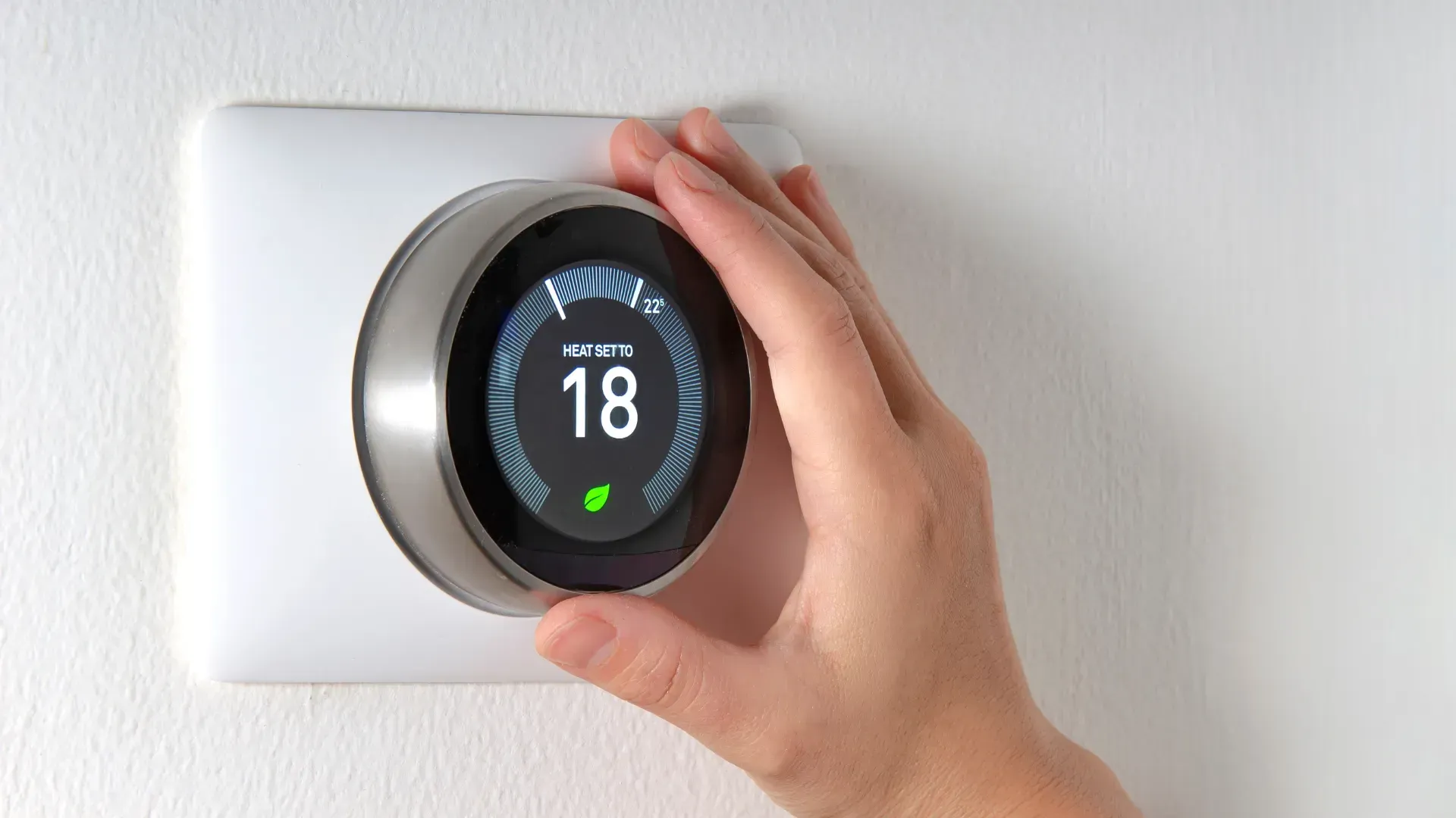 A person is adjusting a smart thermostat on a wall.