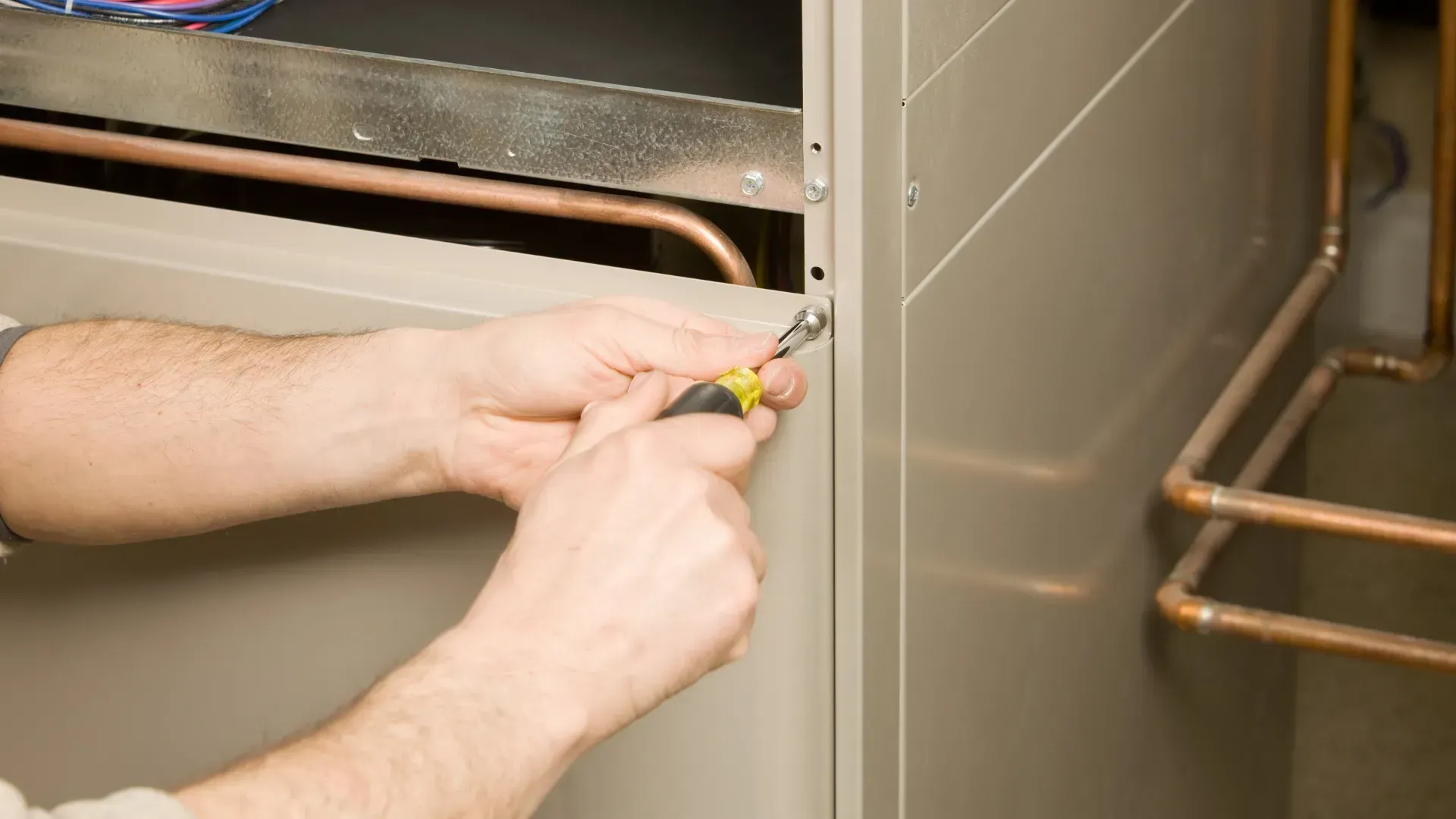 A man is working on an air conditioner with a screwdriver.