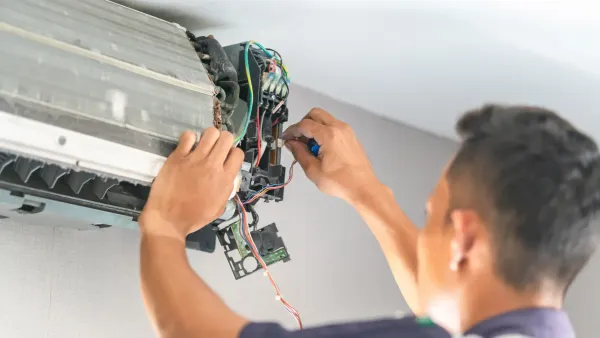A man is fixing an air conditioner with a screwdriver.