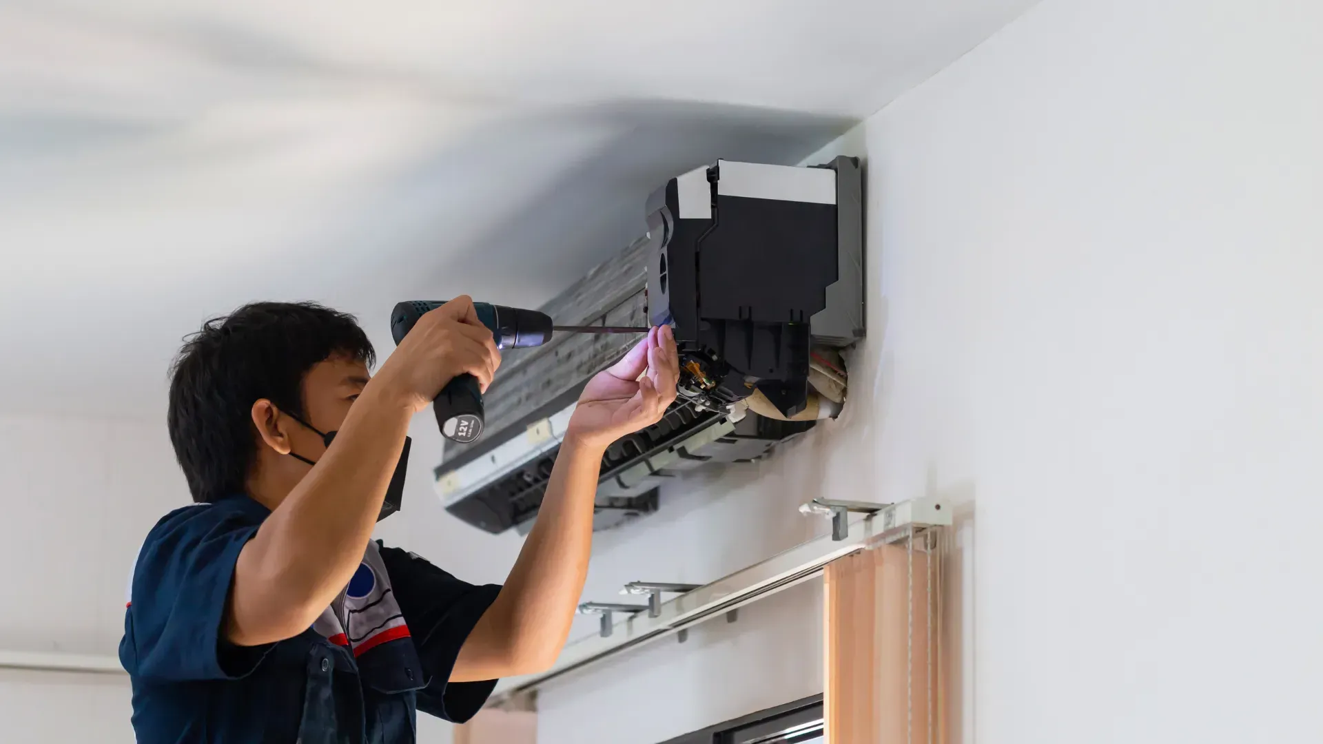A man is fixing an air conditioner with a screwdriver.