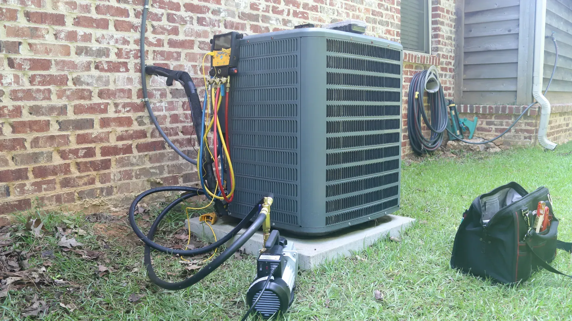 An air conditioner is being repaired in the backyard of a brick house.