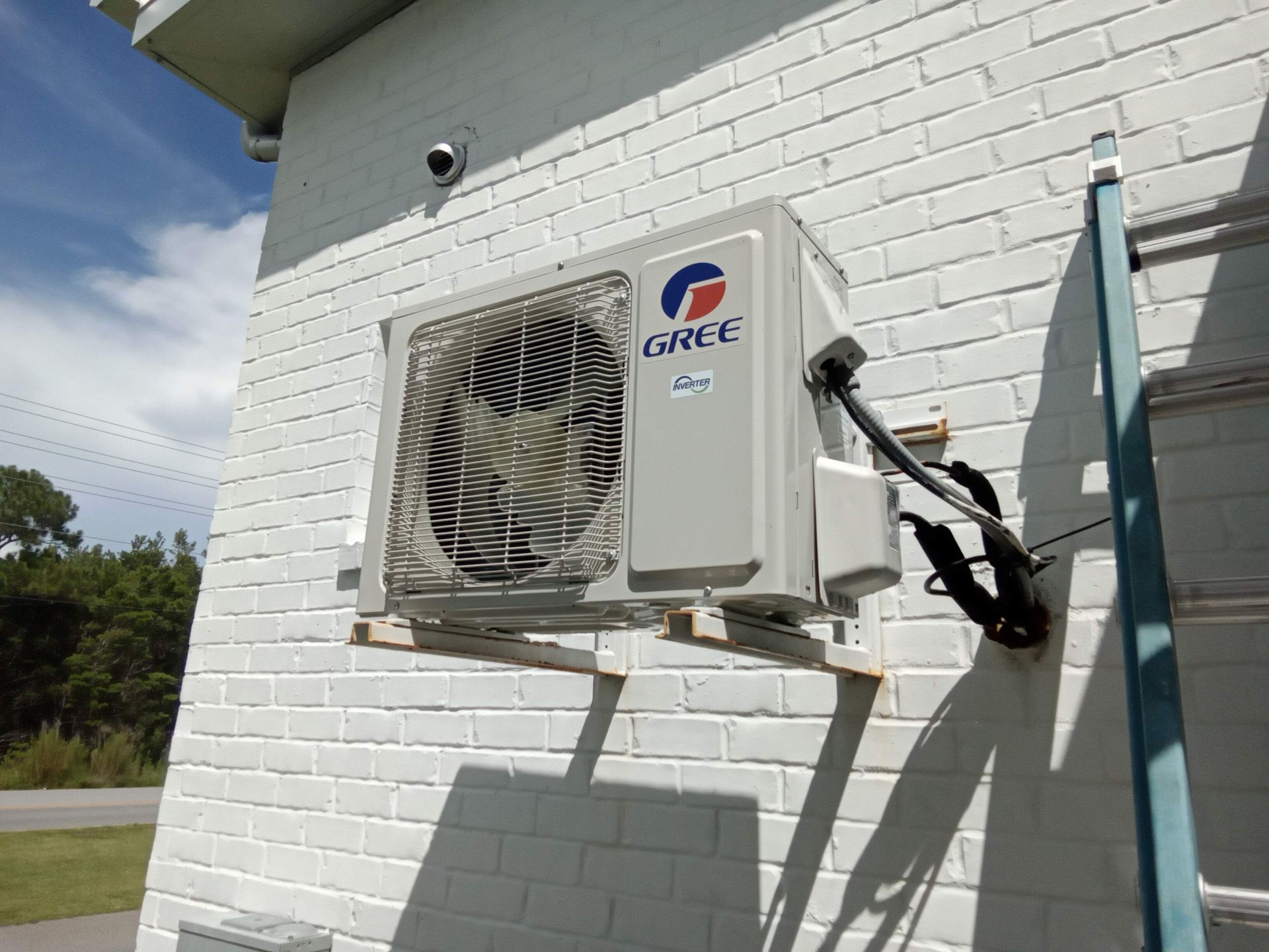 A gree air conditioner is mounted on a white brick wall