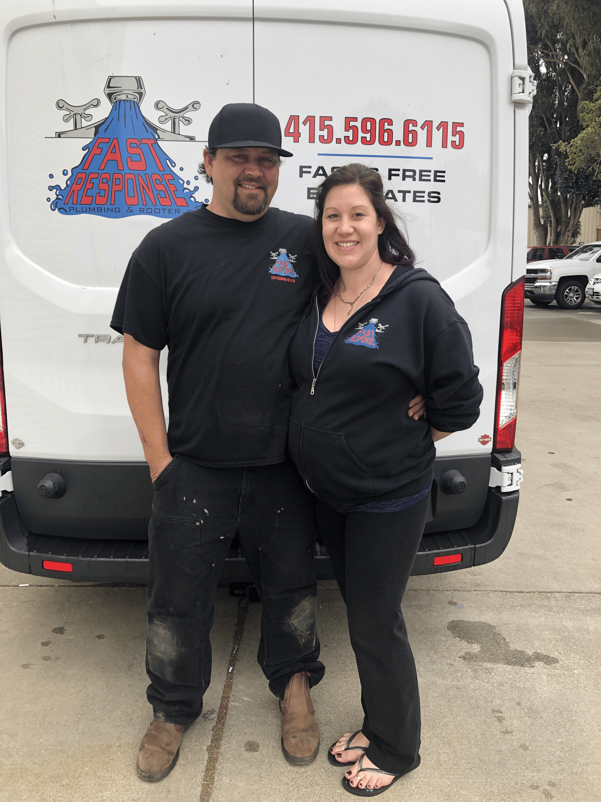 Two smiling people stand in front of a white service van with a red logo and phone number.