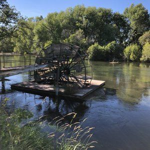 A water wheel is sitting on a raft in the middle of a river.