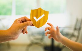 A person is holding a paper shield with a check mark on it.